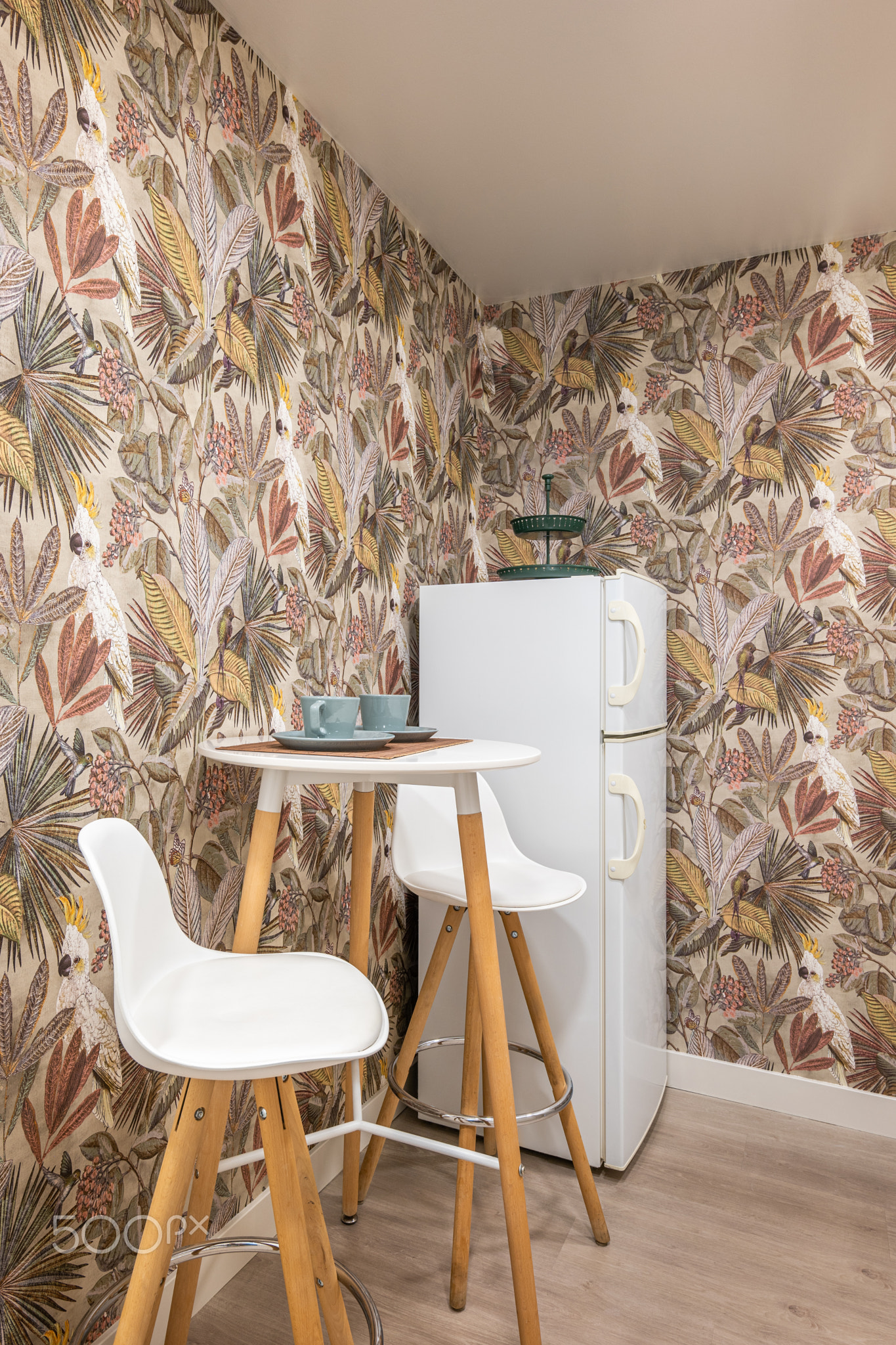 Compact high small round table with cups and two bar stools in the kitchen on the backdrop of boho