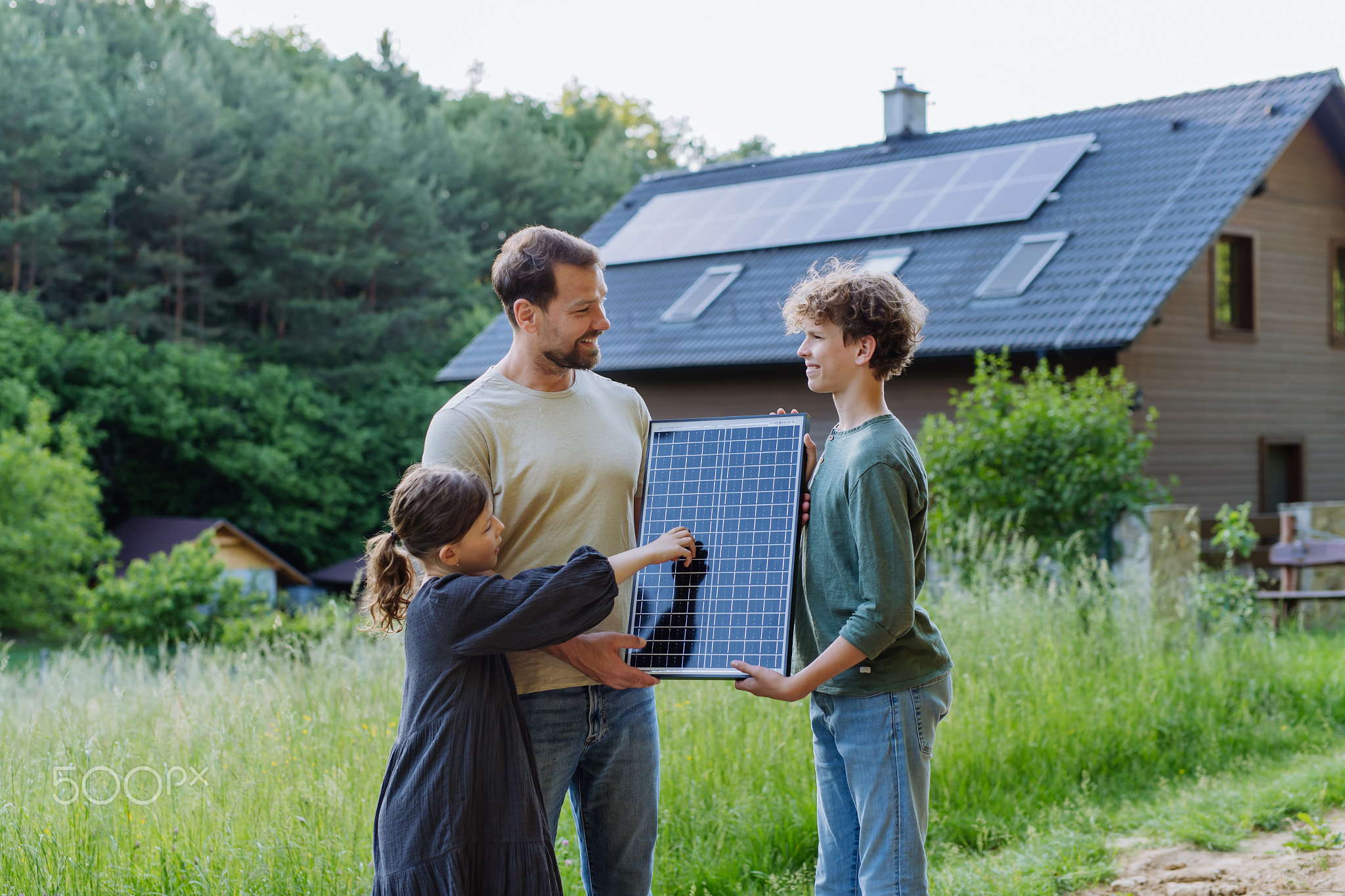 Father and his children holding solar panl standing in front of their house with photovoltaics on