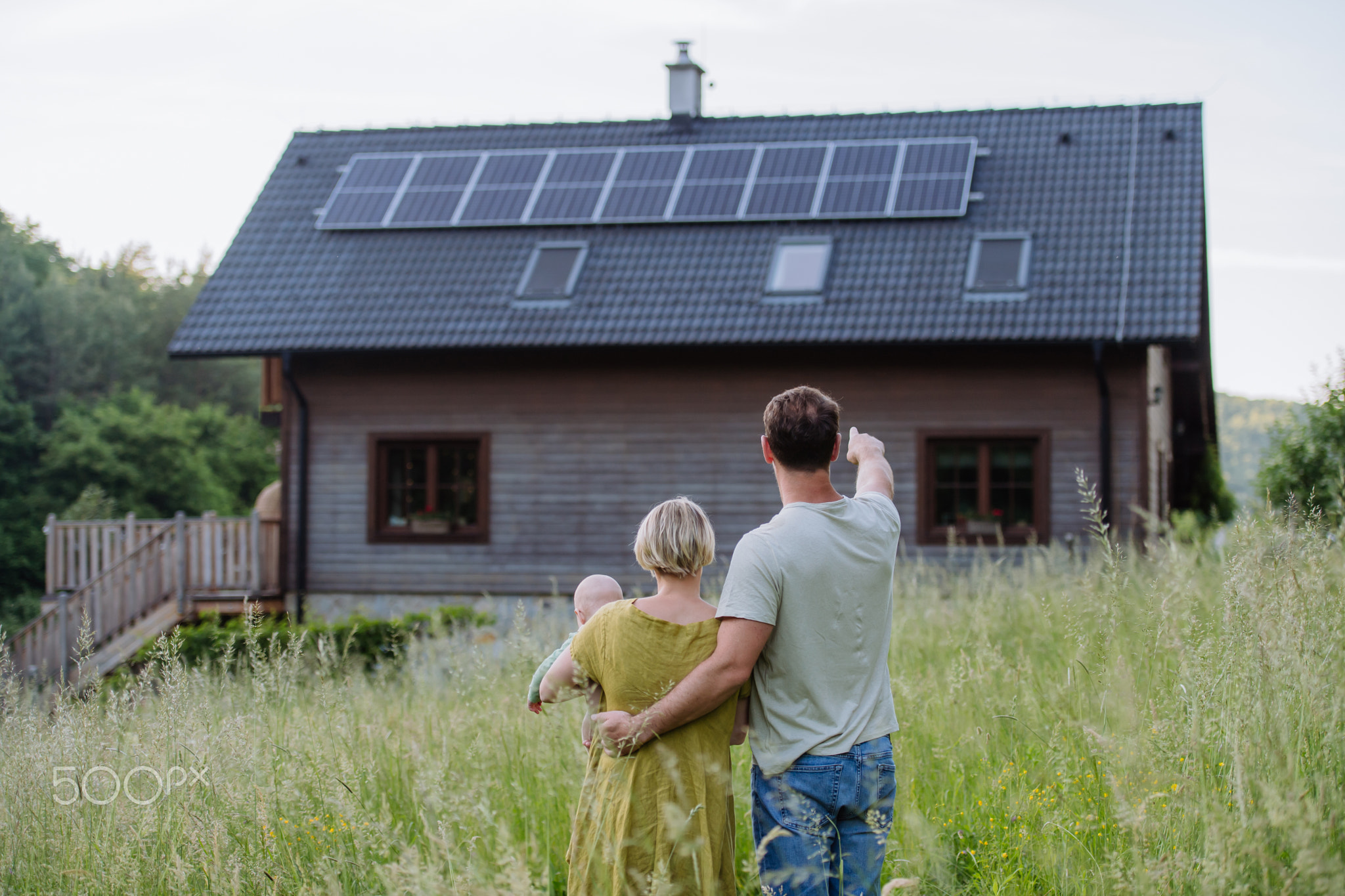 Rear view of family near their house with solar panels. Alternative energy, saving resources and