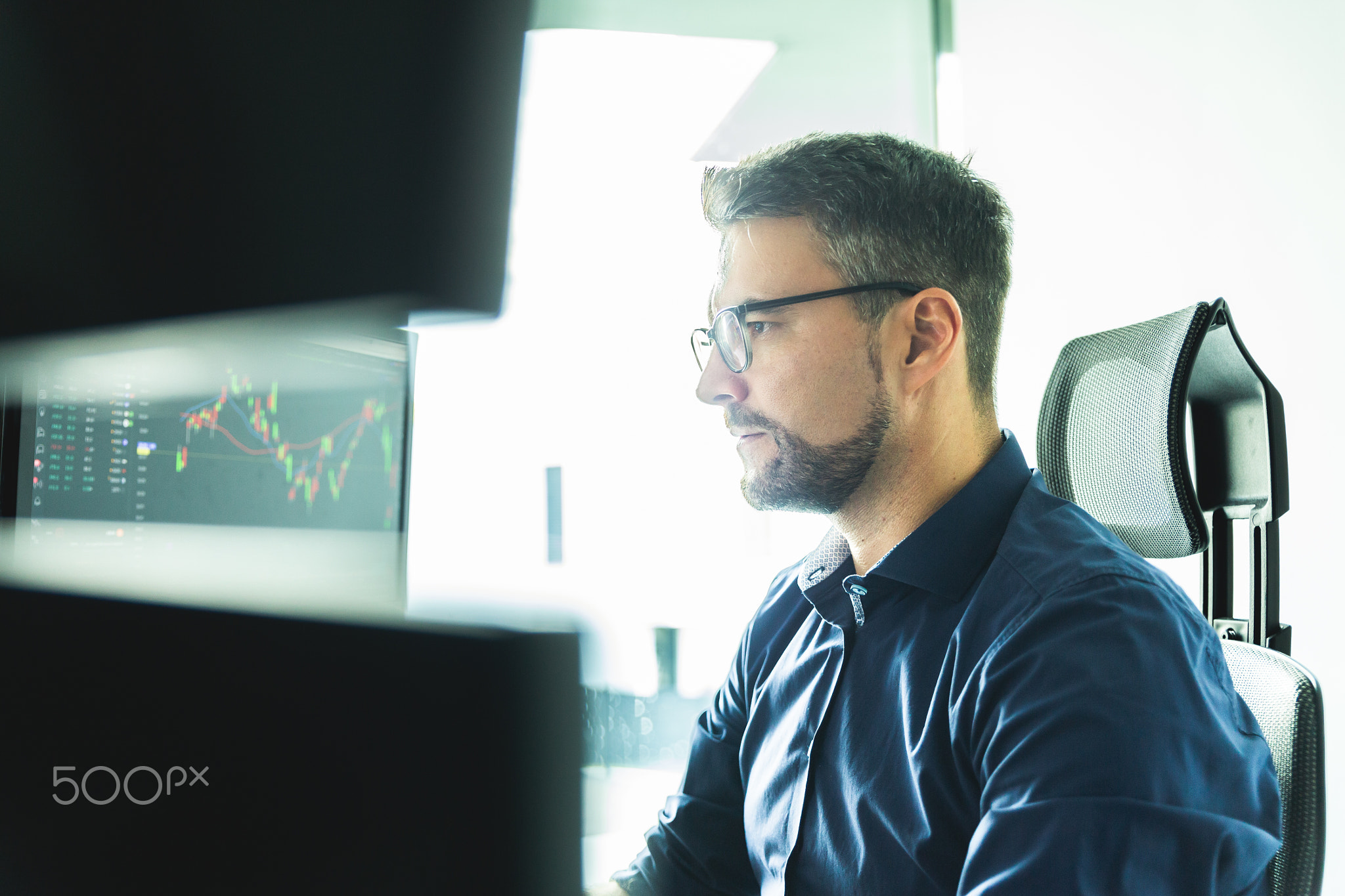 Stock broker trading online watching charts and data analyses on multiple computer screens.