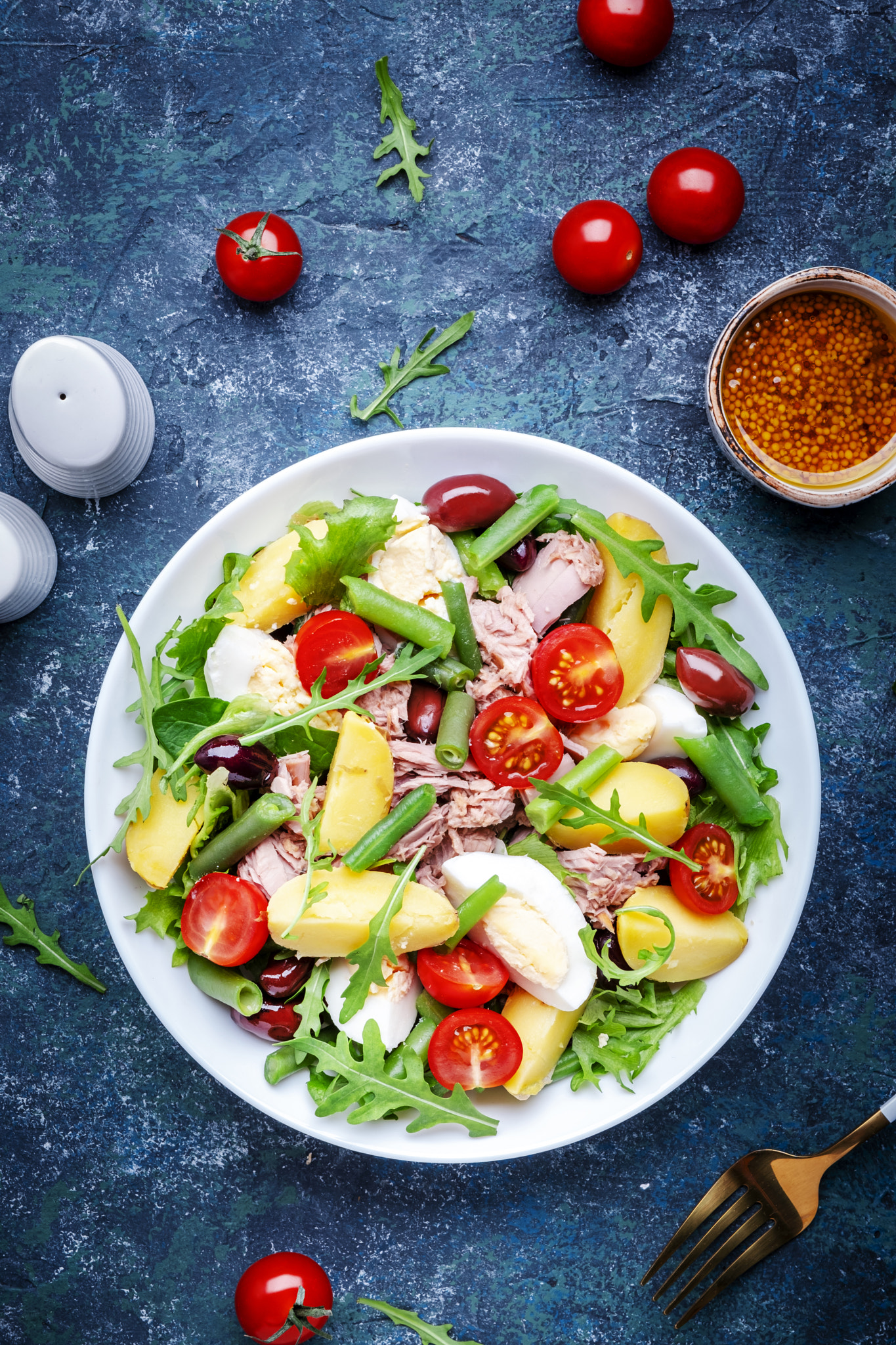 Nicoise salad with tuna, tomatoes, eggs, green beans, potatoes and olives on plate, blue table backg