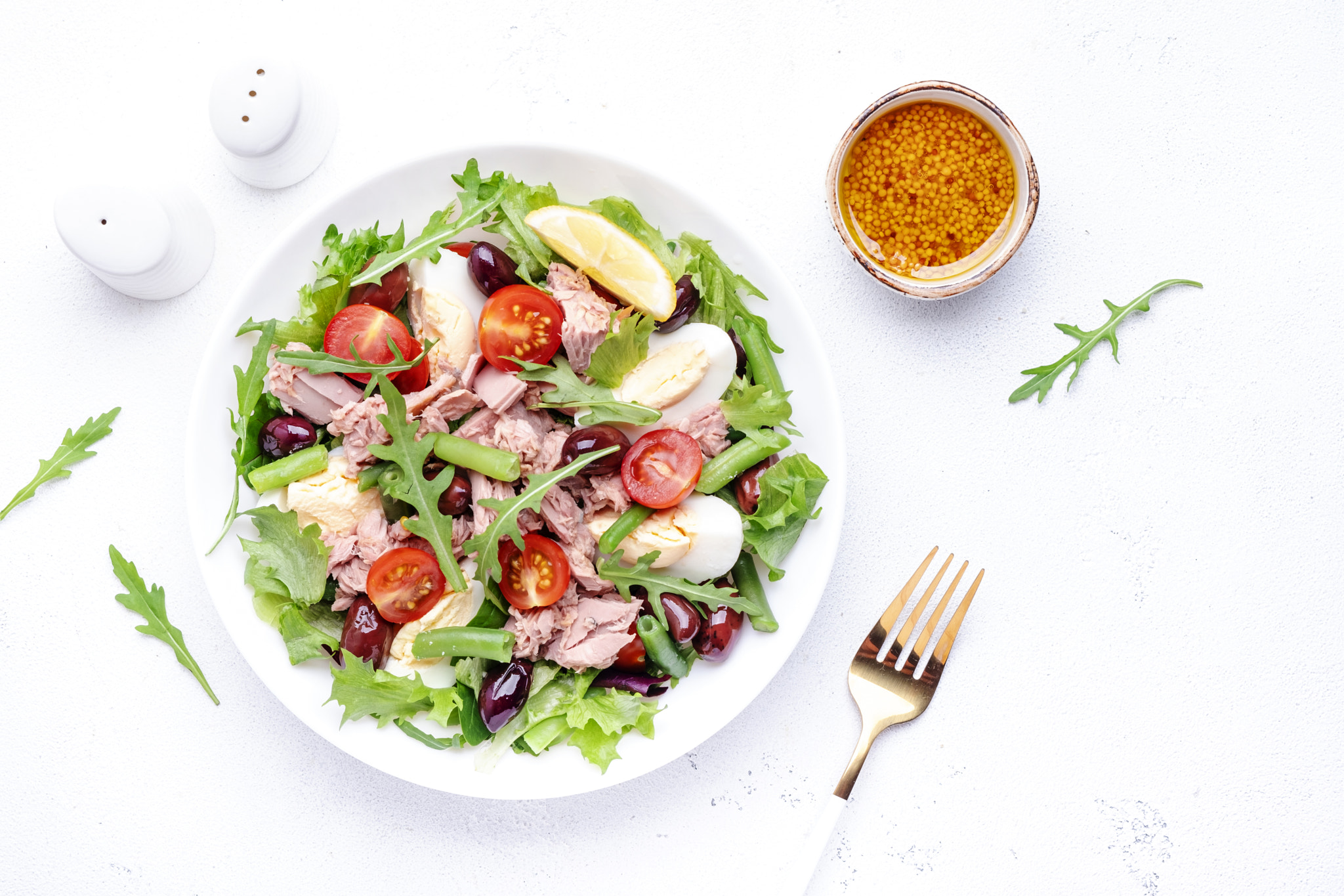 Nicoise salad with tuna, red tomatoes, boiled eggs, green beans and olives on plate, white table bac