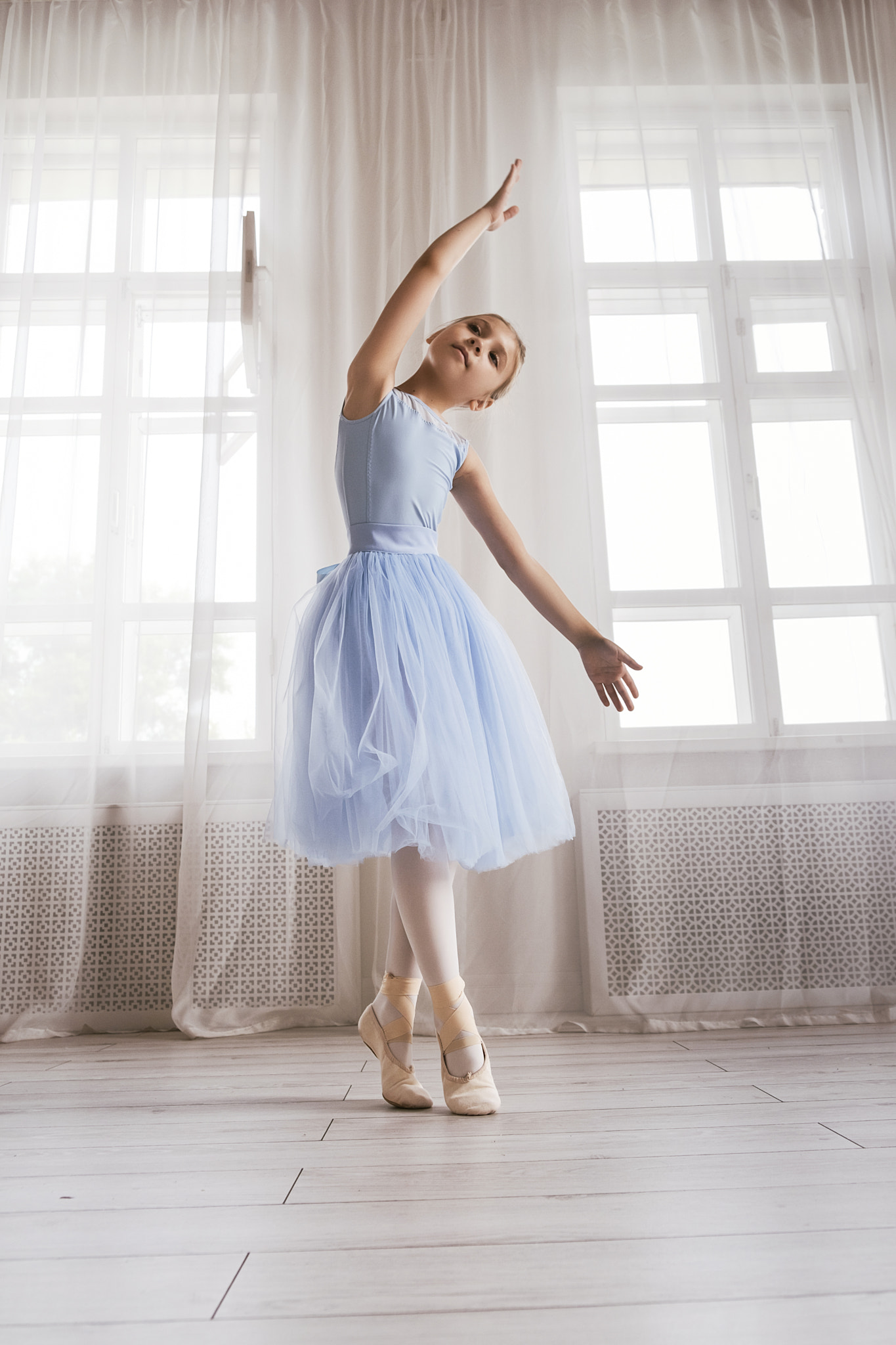 ballerina girl in a blue bodysuit and skirt shows ballet steps