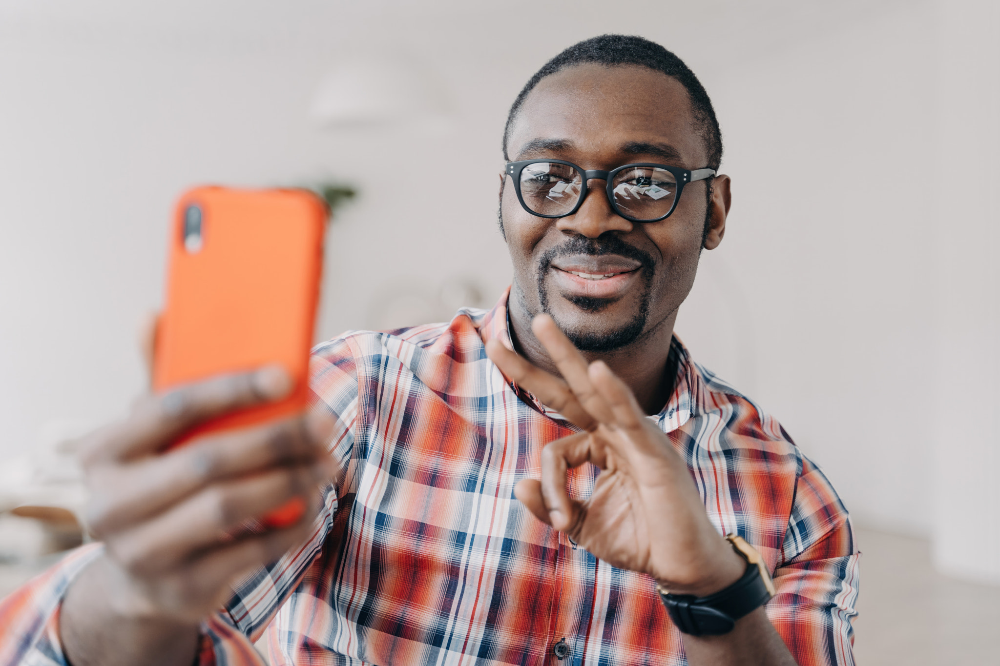 Smiling African-American man in glasses shows okay sign, communicates on video call, holds smartphon