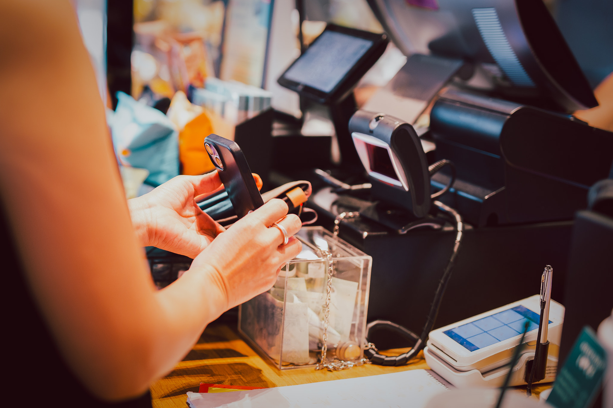 Woman scanning QR code payment via mobile phone at cashier in cafe.