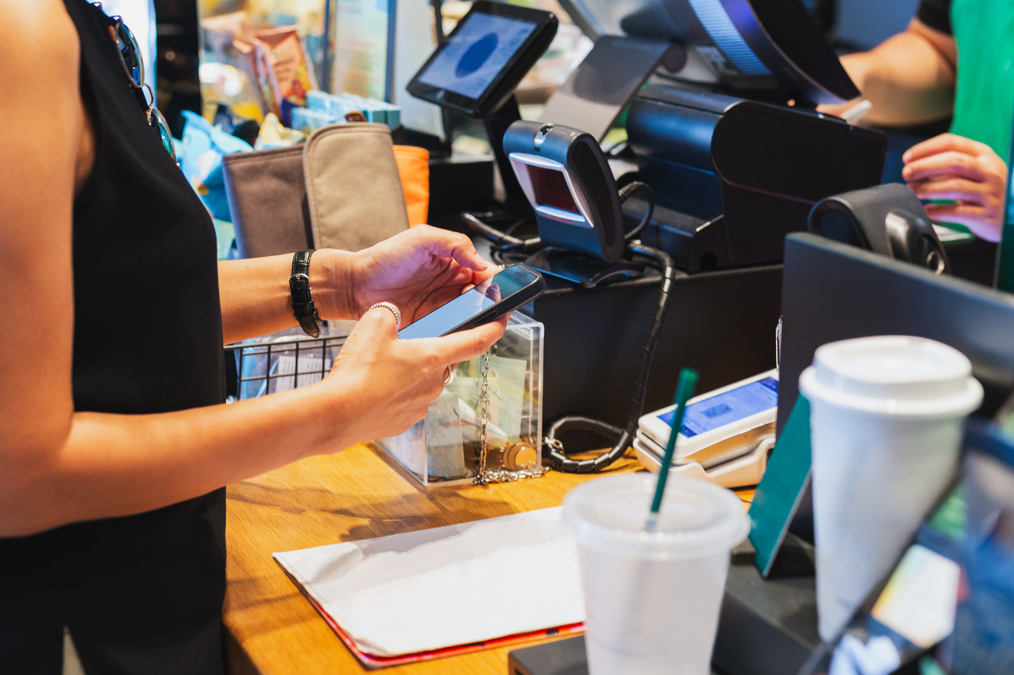 Woman scanning QR code payment via mobile phone at cashier in cafe.