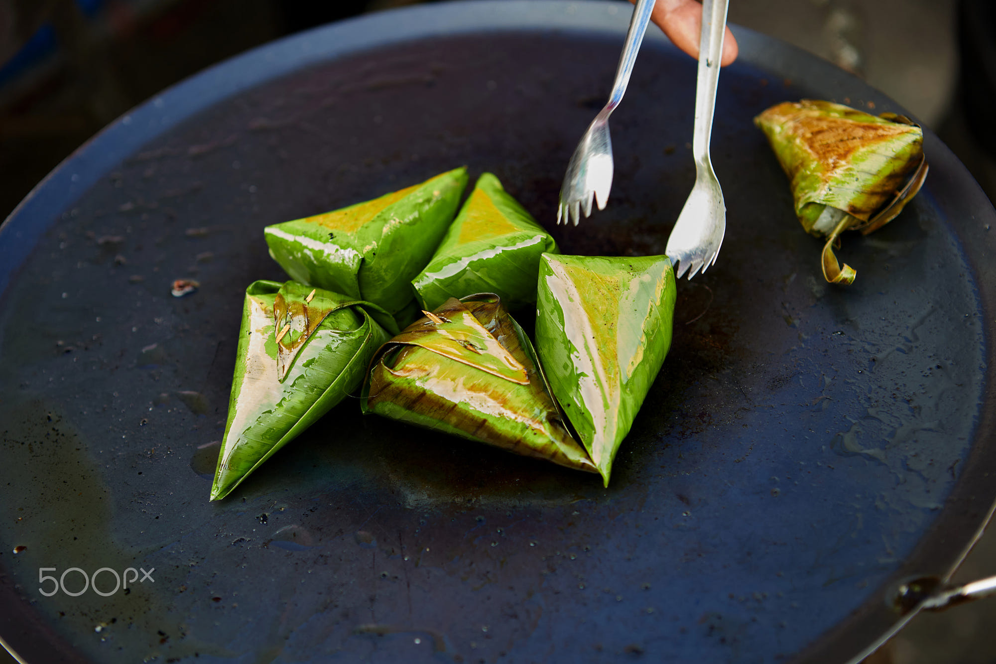 Grilling the stuffed sticky rice wrapped with banana leaf on a pan: Grilling the stuffed sticky rice wrapped with banana leaf on a pan
