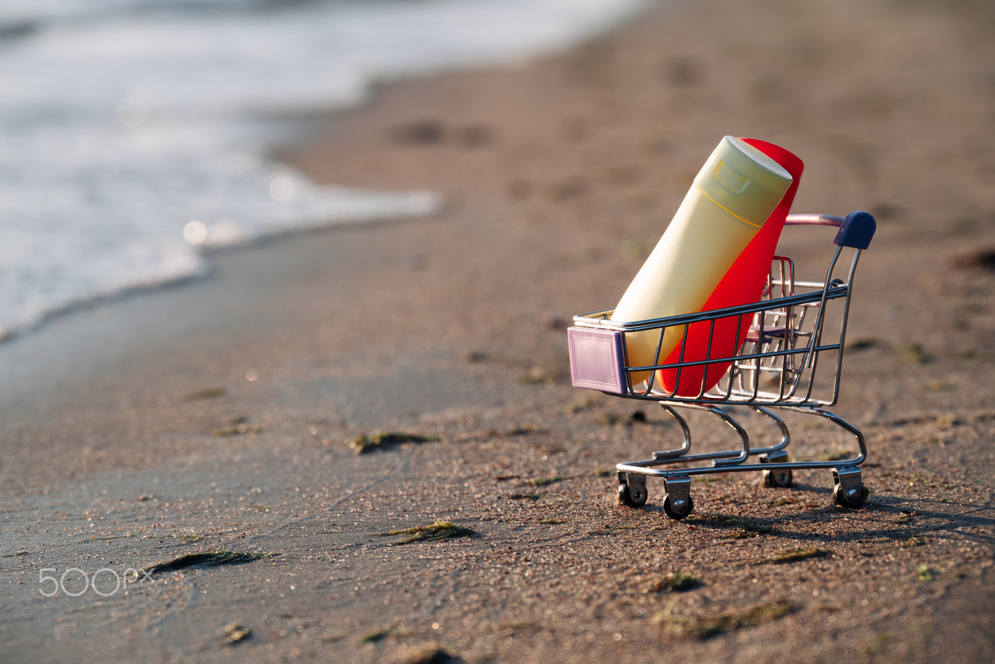 On Sand Is Miniature Shopping Cart With Jars Of Sunburn, Concept Of