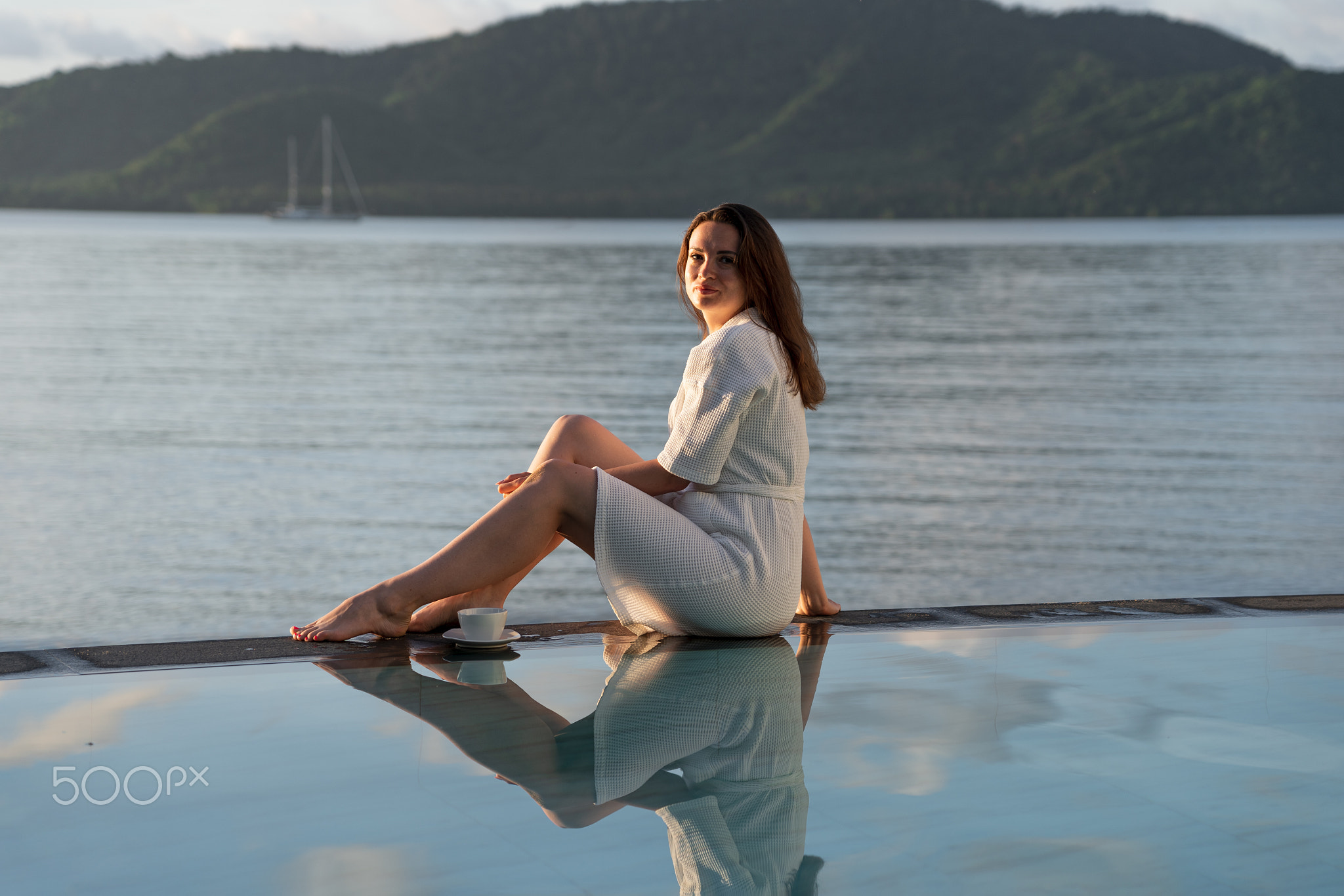 brunette white bathrobe sits at edge of pool overlooking Indian Ocean