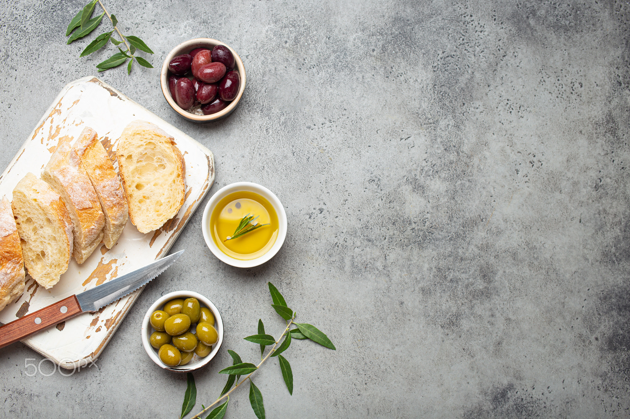 Sliced fresh ciabatta on cutting kitchen board, green and brown olives