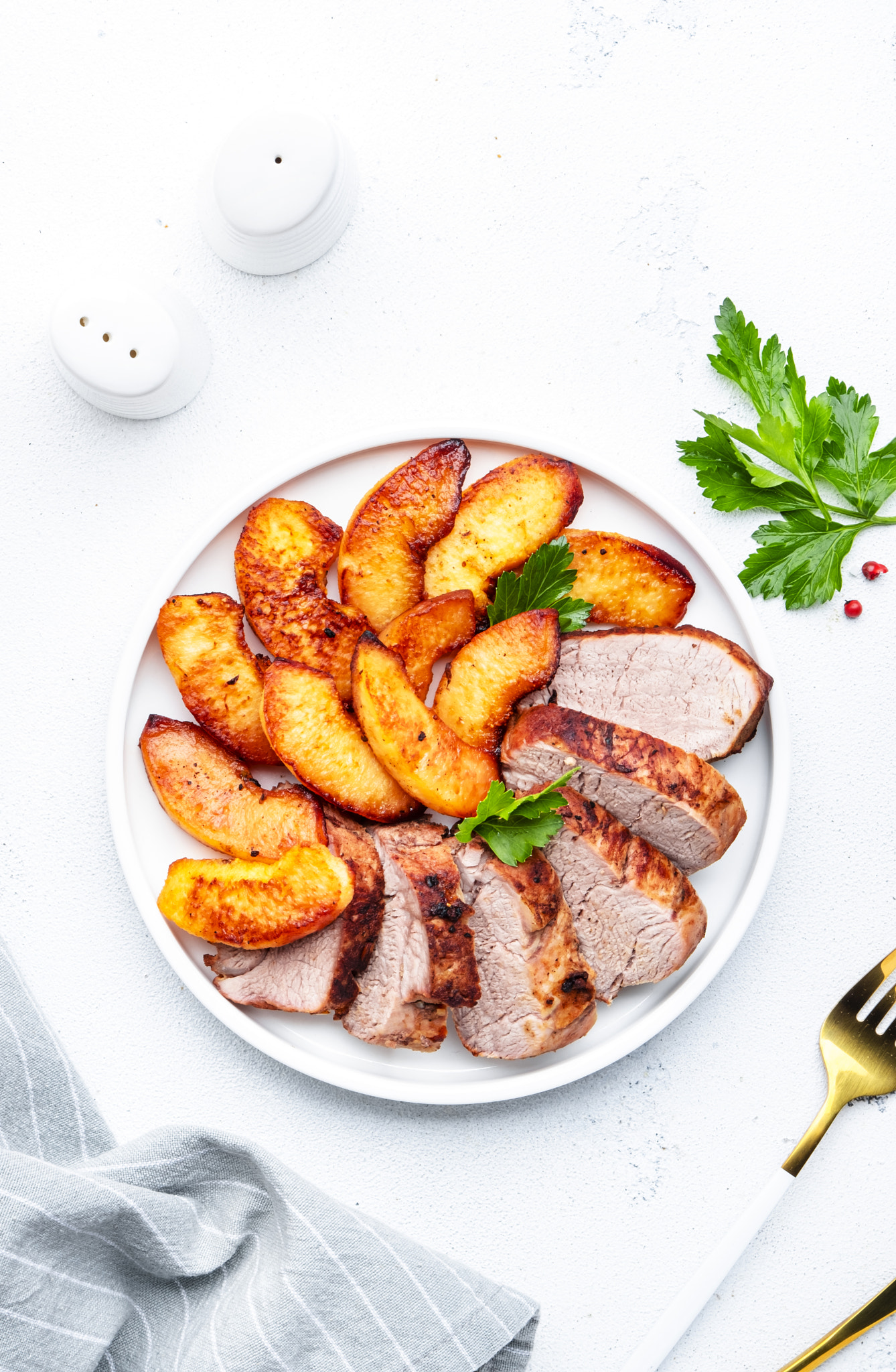 Baked pork tenderloin and quince or apple slices with parsley served on white plate. White table bac