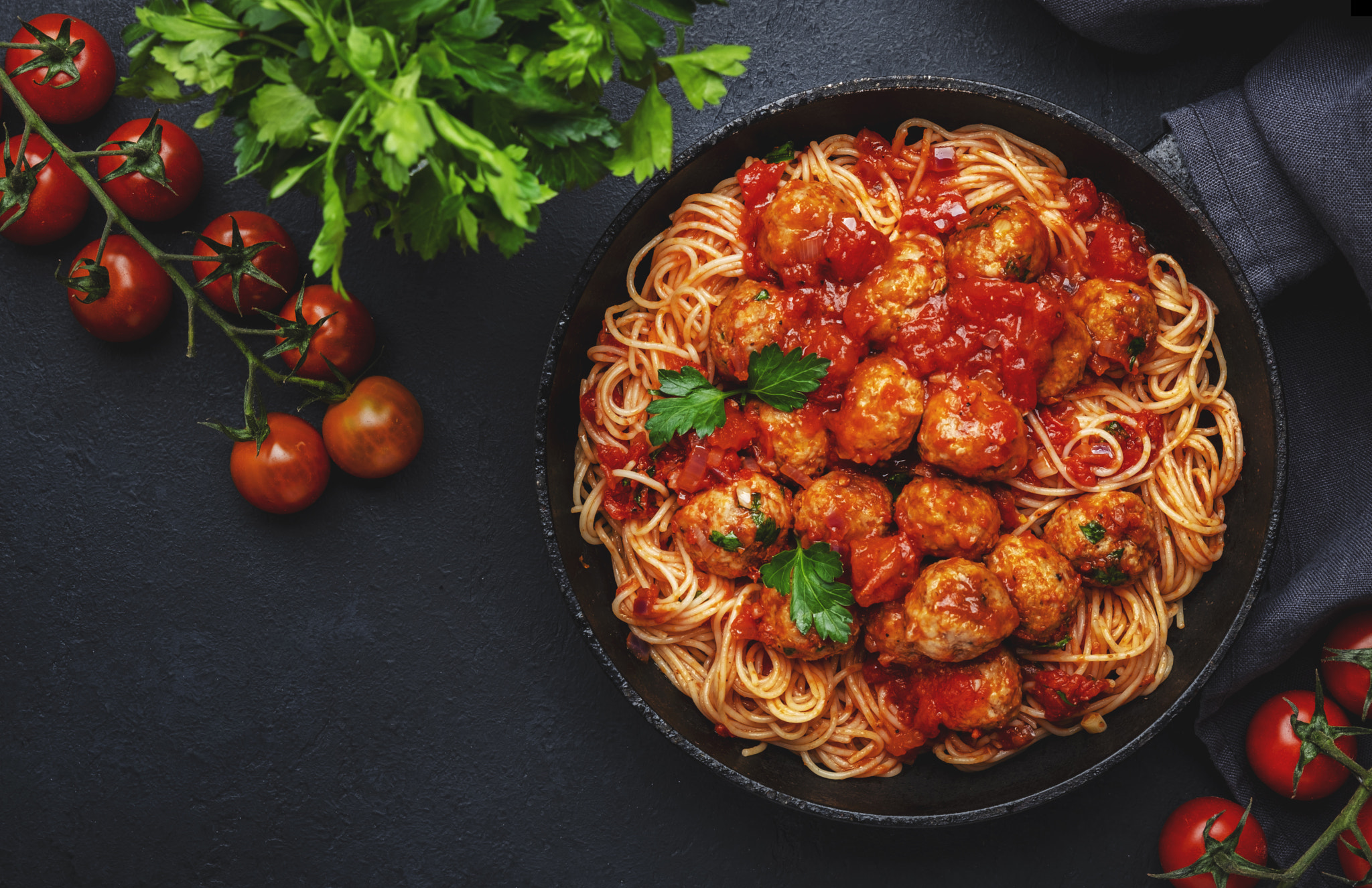 Spaghetti pasta with meatballs in tomato sauce with parsley in frying pan, dark table background, to