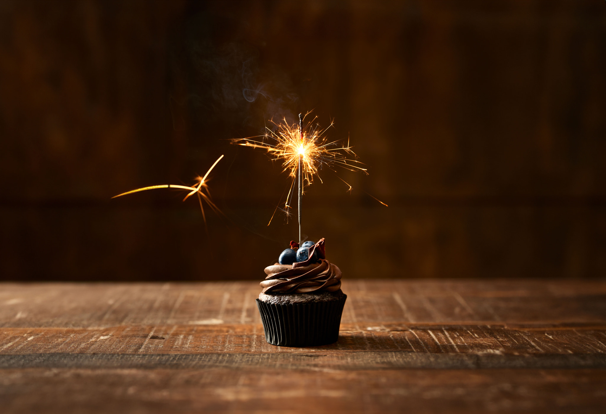 Chocolate cupcake with a sparkler on the table and brown background