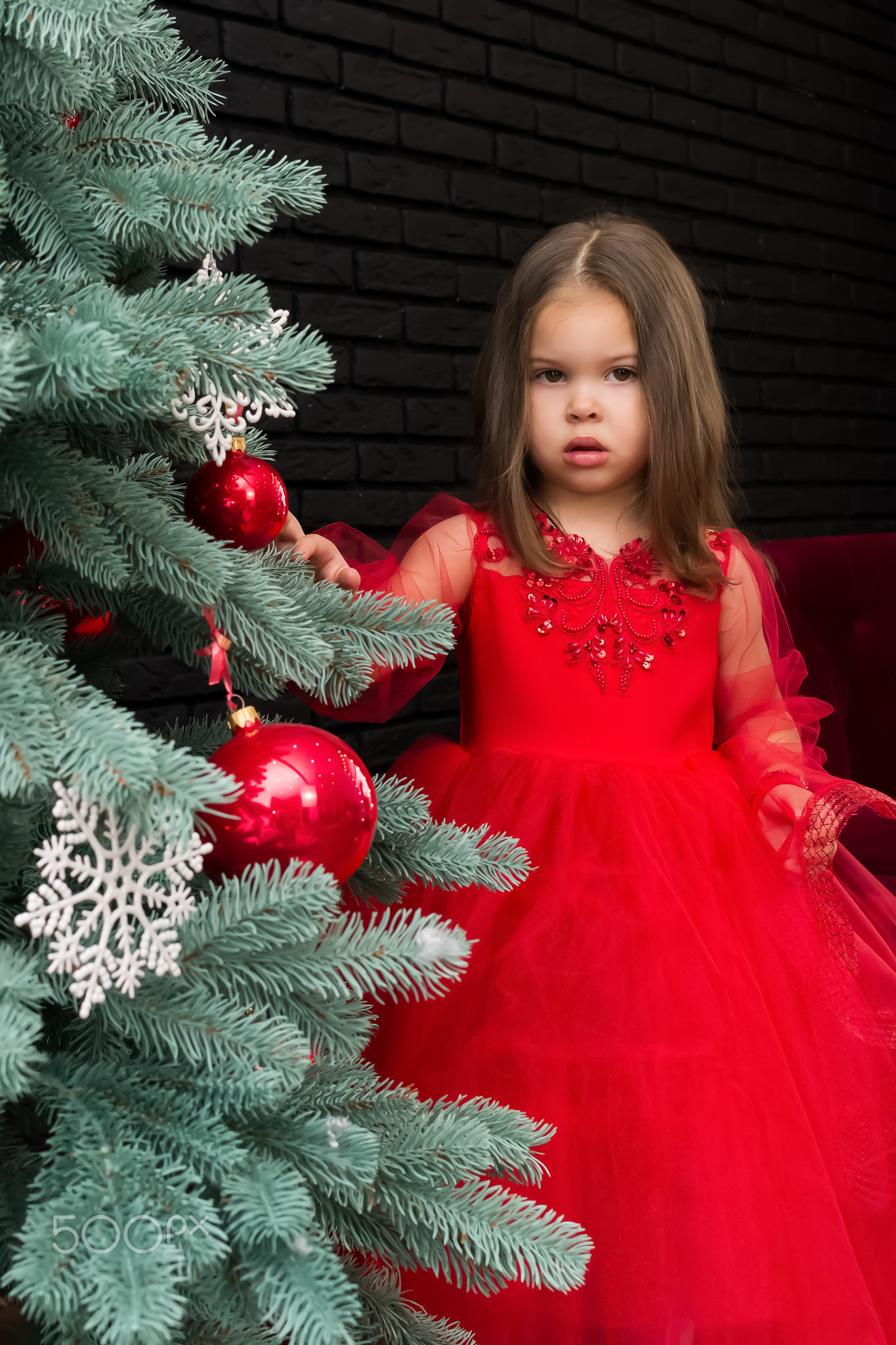 Little girl in red dress smiling by Christmas tree. Little beautiful girl in a red evening dress the