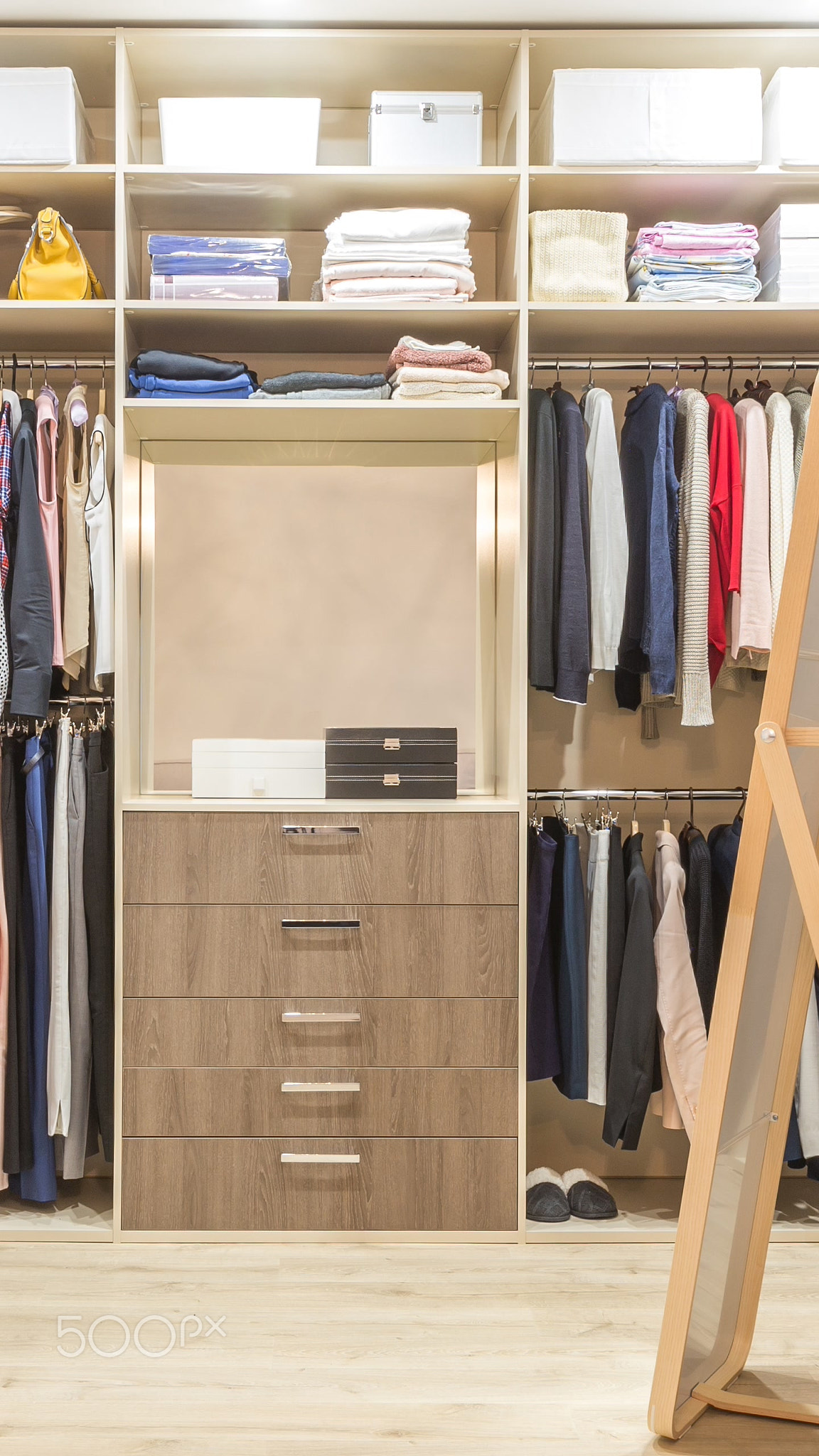 Modern wooden wardrobe with clothes hanging on rail in walk in closet