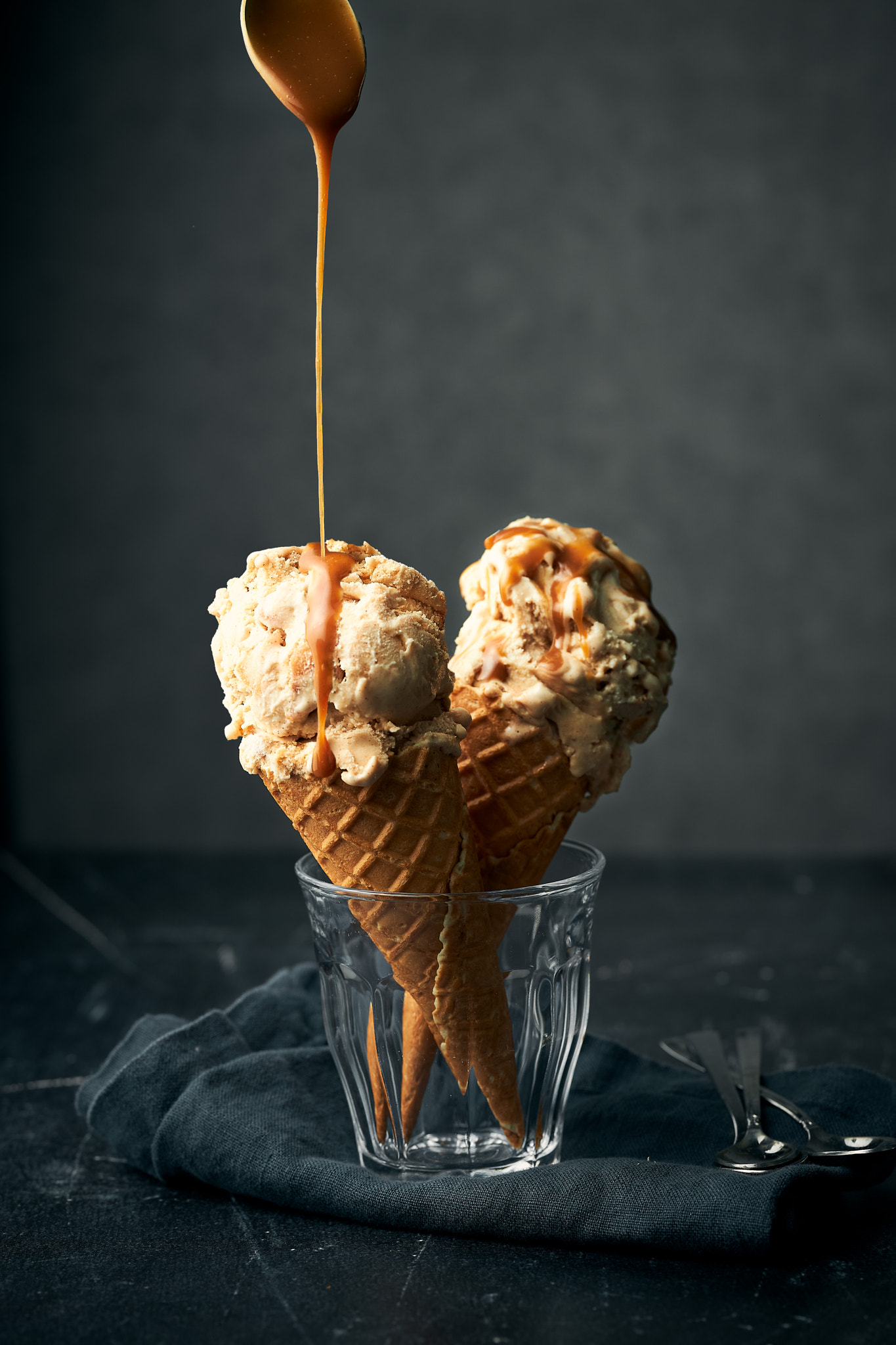 Warm caramel sauce poured over caramel ice cream on a black background surrounded by dark props