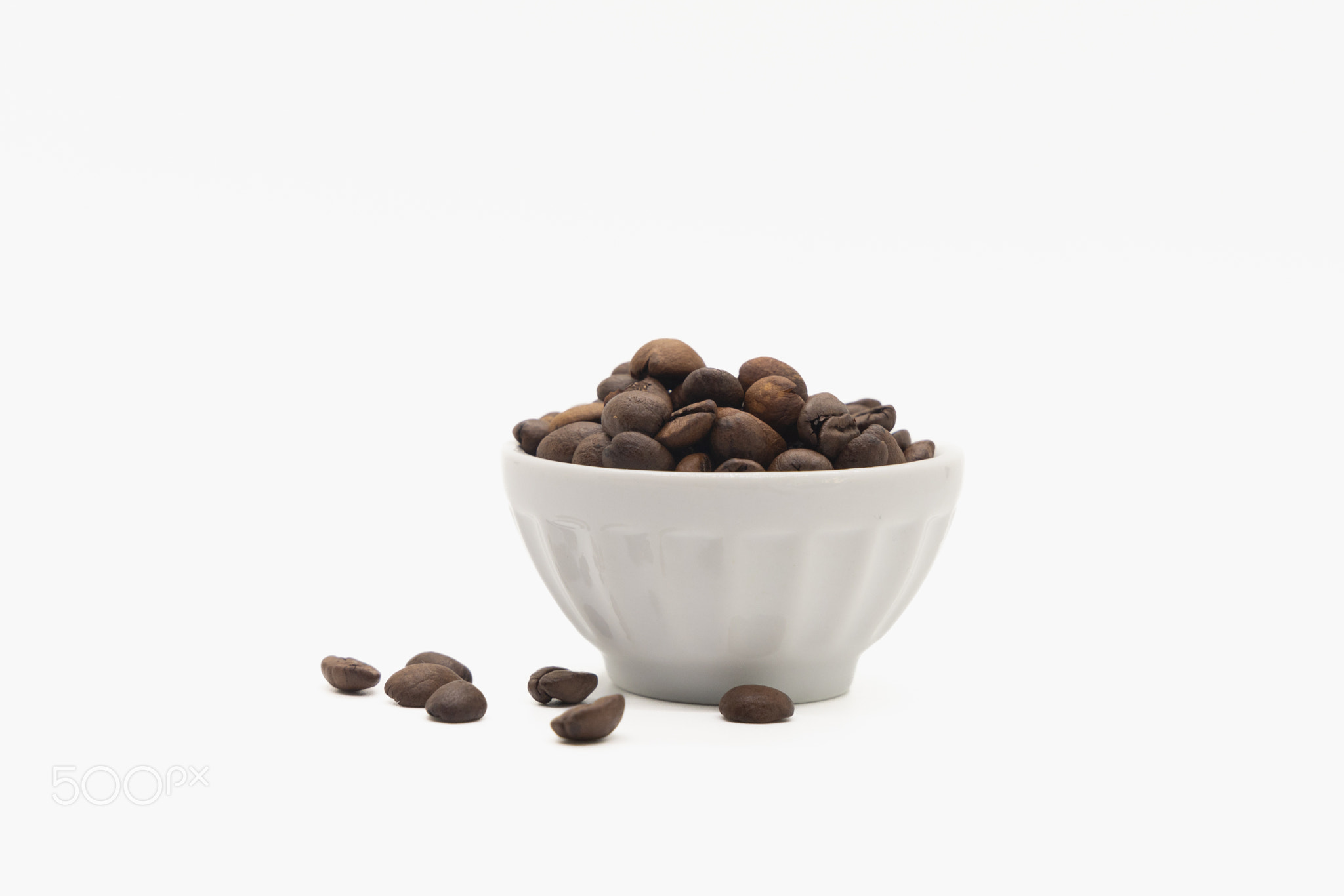 coffee beans in a white bowl and scattered on the isolated background