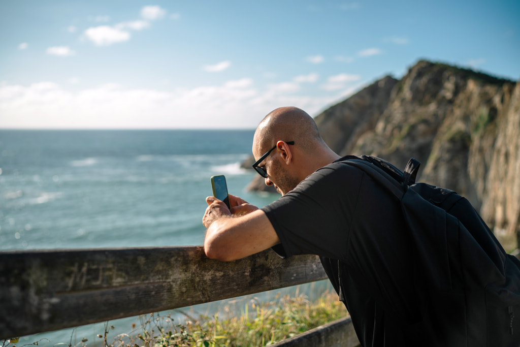 Man using mobile phone while standing by railing against sea by Olha Dobosh on 500px.com