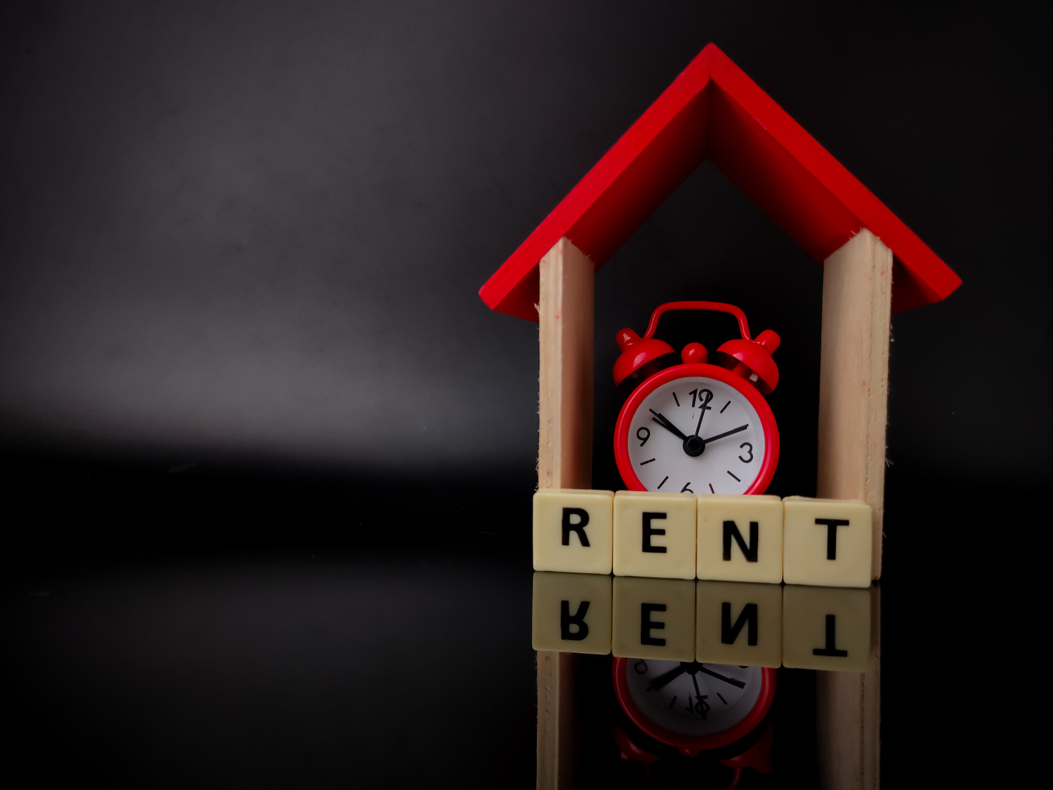 Wooden house and clock with word RENT on black background with reflection, Wooden house and clock wi