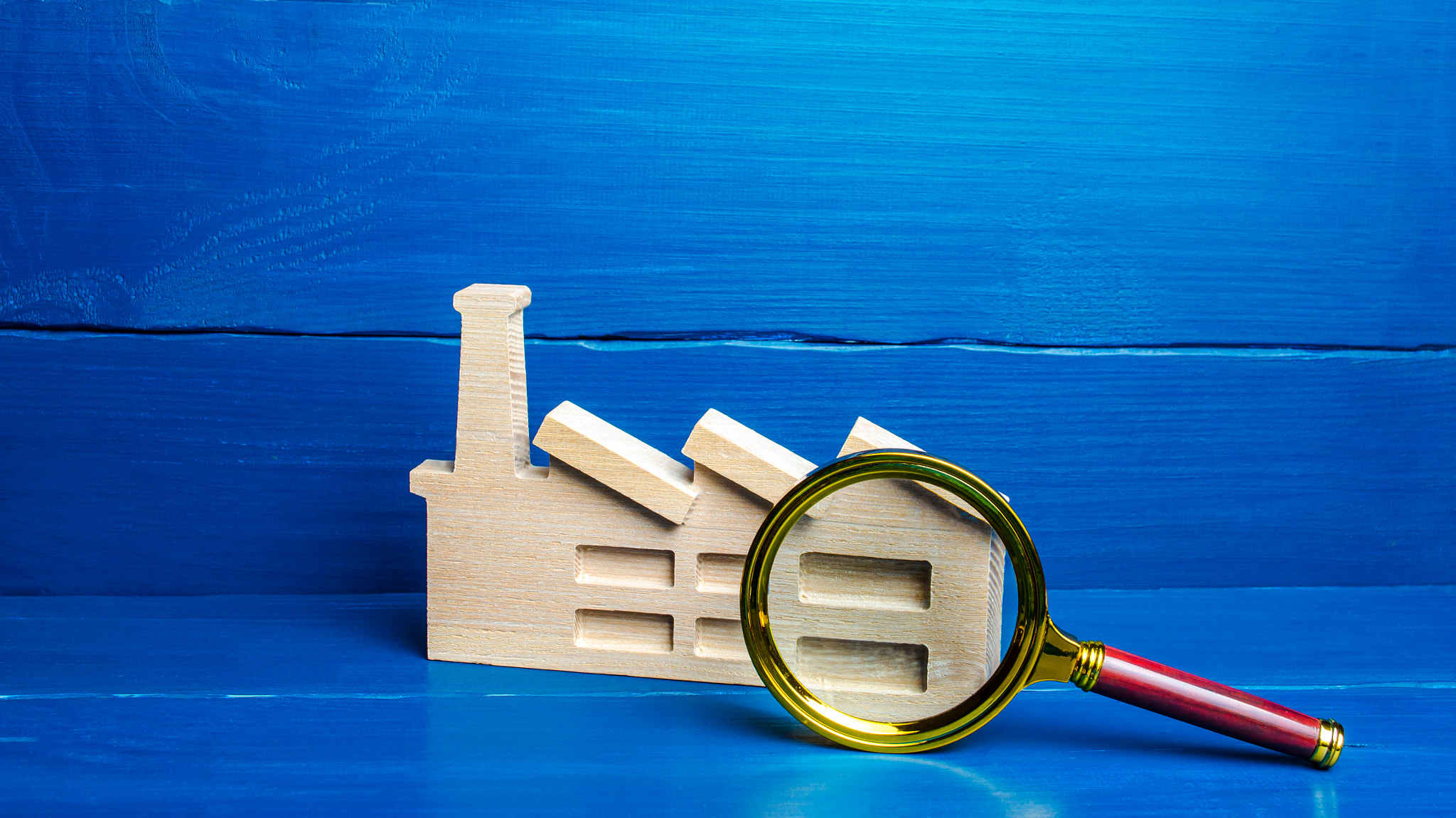 Figurine of an industrial factory plant and a magnifying glass. Big business monitoring concept, emi