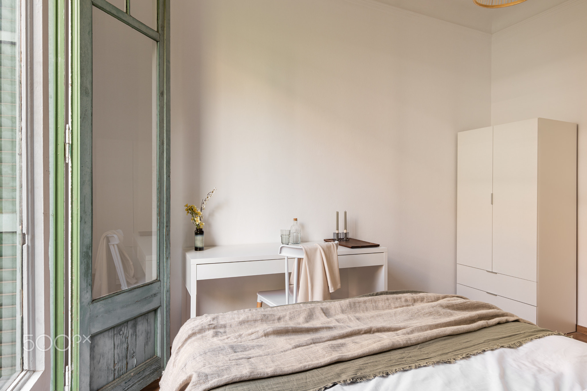 Nice and cozy hotel room with a double bed with a wardrobe and a table in light beige tones. The