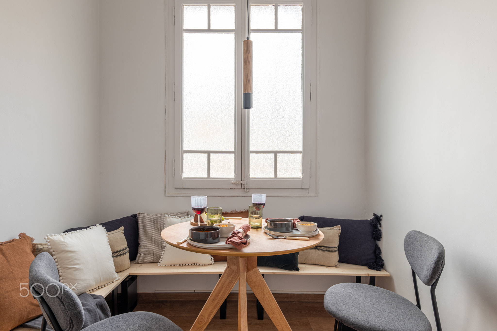 Horizontal shot breakfast for two with wine on a wooden round table gray chairs and a corner bench