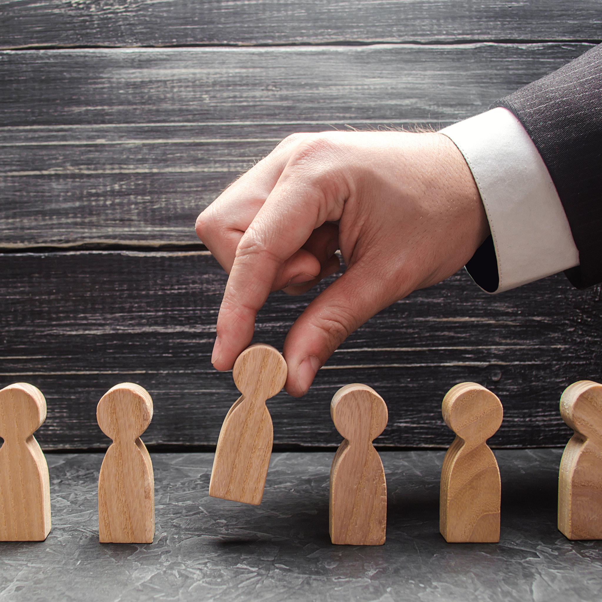hand of a businessman takes a wooden figure of a man. The concept of search, hiring and firing worke