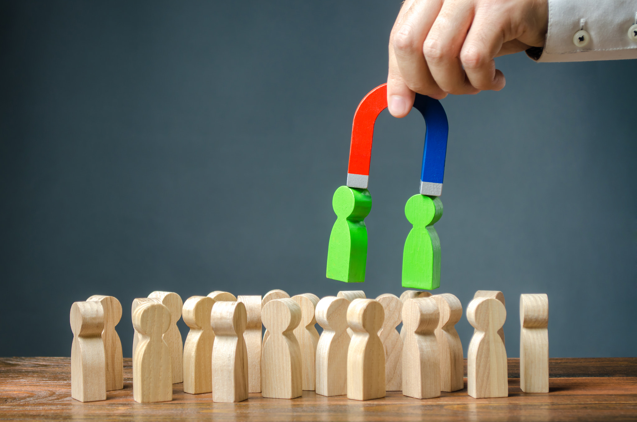 Businessman with a magnet pulls green figures of people out of the crowd. Recruiting new workers. Se