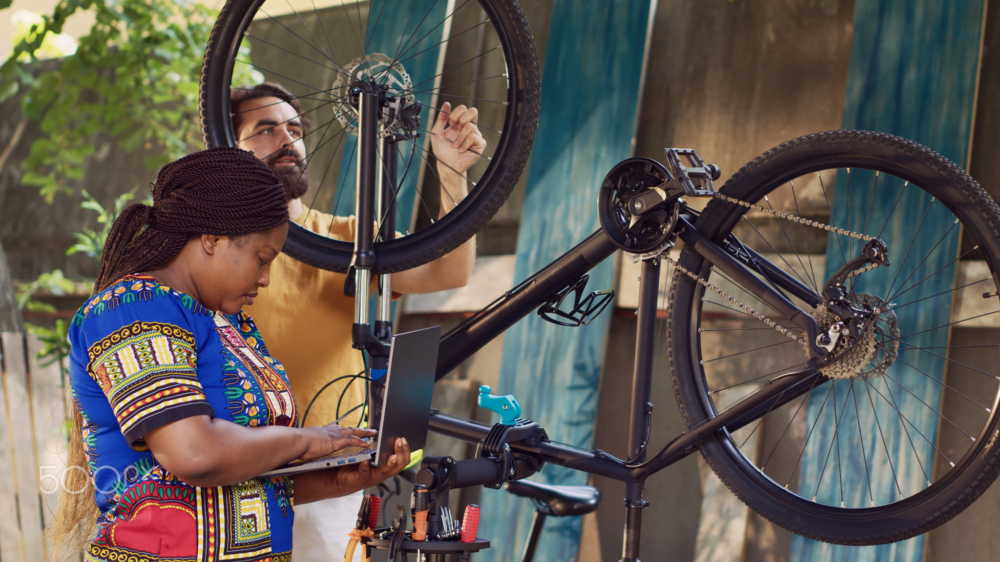 Black woman fixing bicycle with laptop