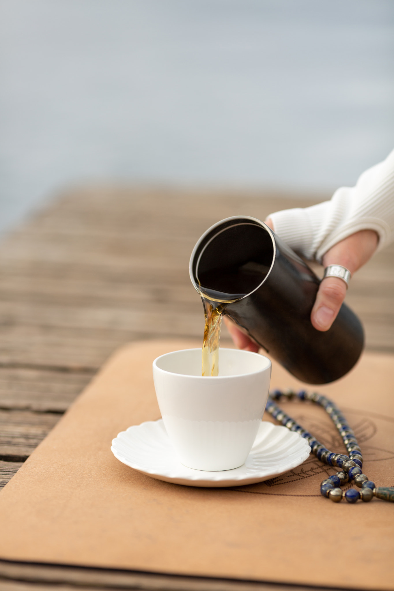 A woman after yoga practice pours herbal tea from a thermos into a white cup, Malas beads are lying