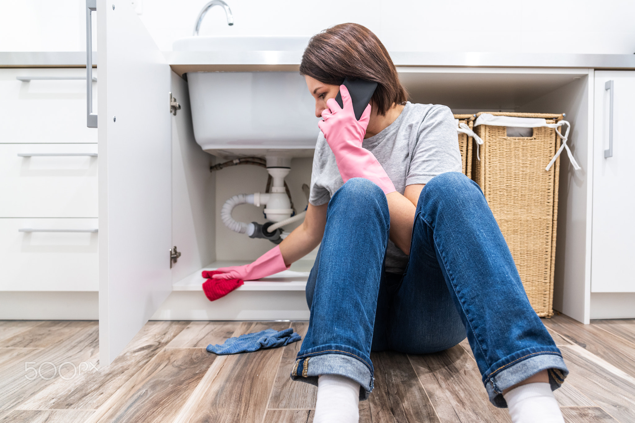 Woman sitting near leaking sink in laundry room calling for help