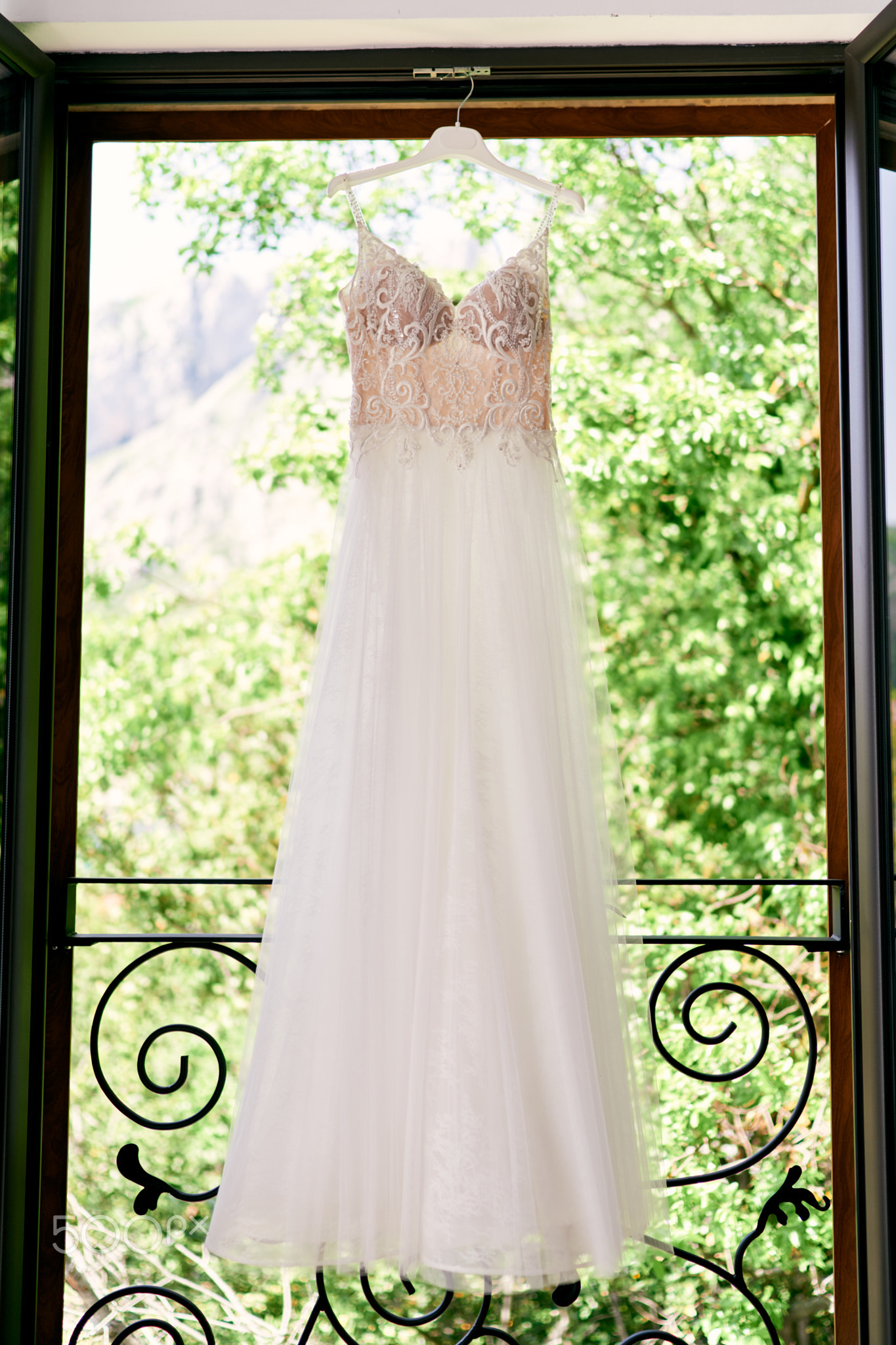 Lace wedding dress hangs on a hanger on the balcony against the