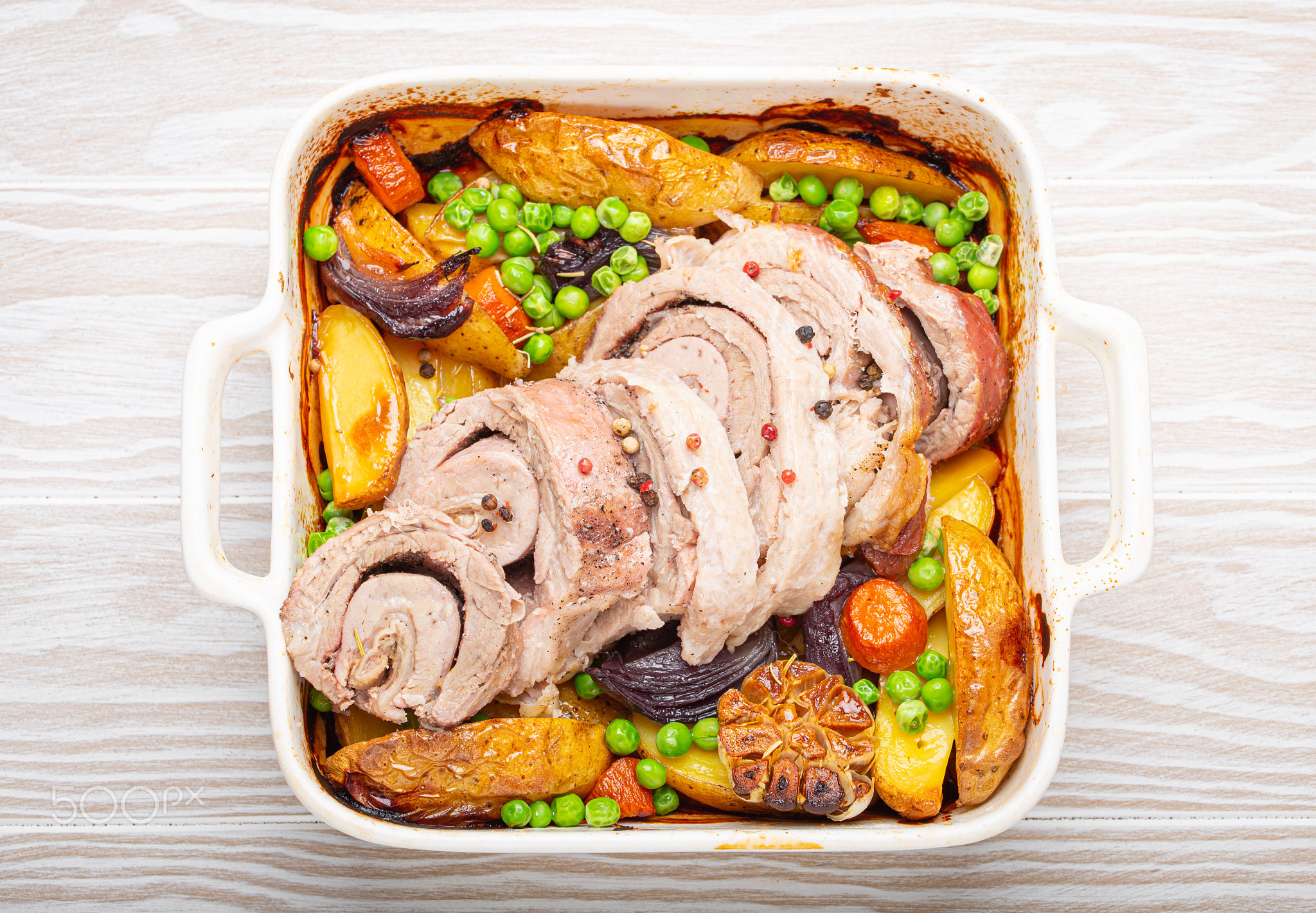 Rolled sliced pork roasted in white casserole dish with potatoes