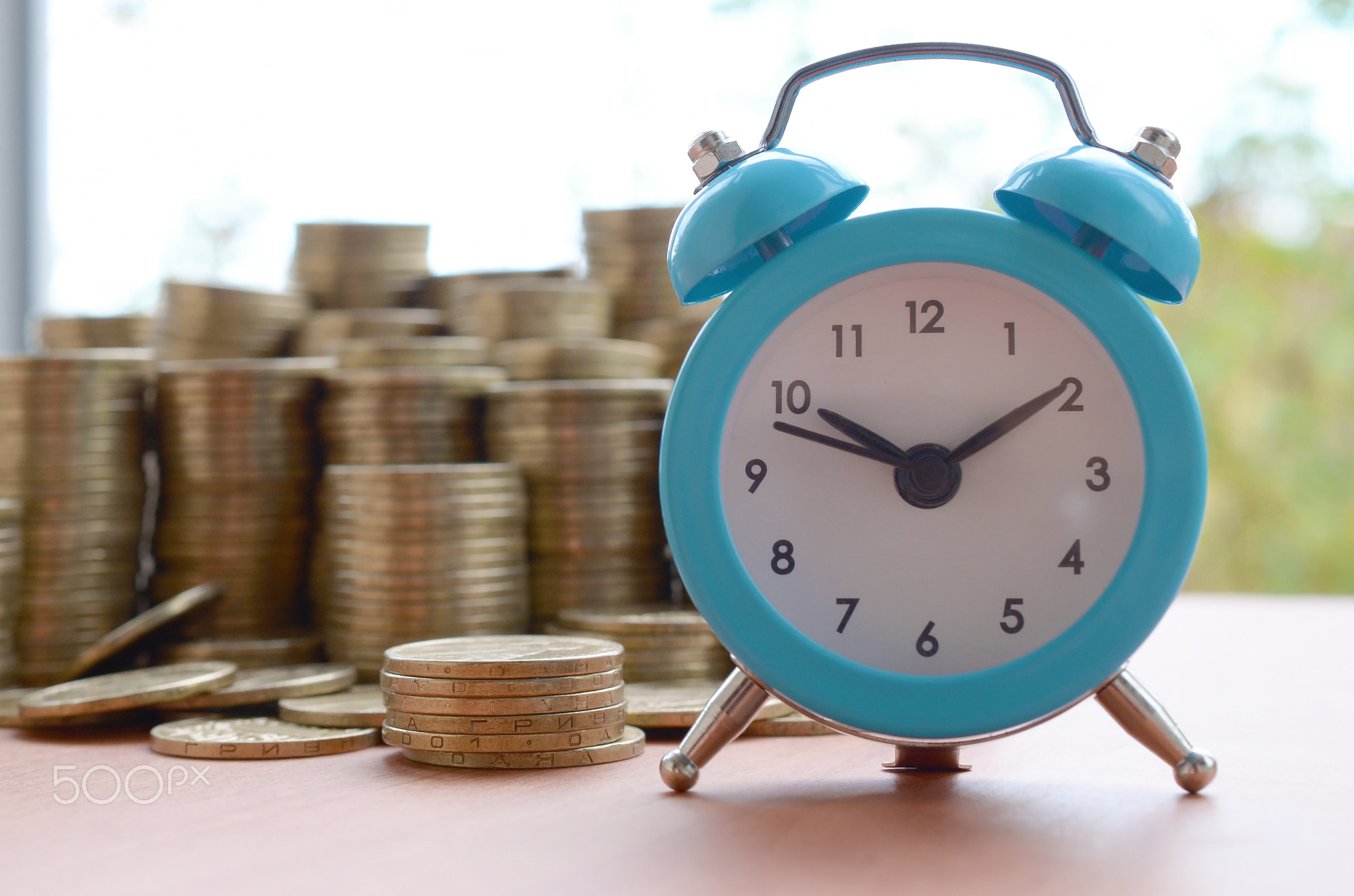Blue alarm clock on big amount of shiny ukrainian old 1 hryvnia coin stacks close up on blurred