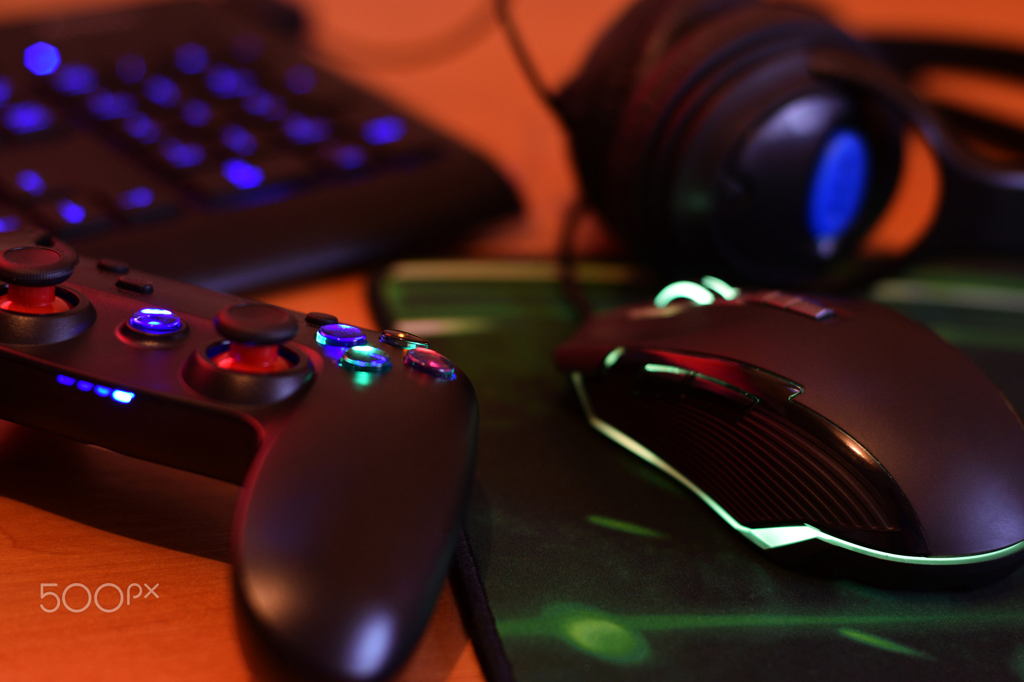 Modern gamepad and gaming mouse lies with keyboard and headphones on table in dark playroom scene