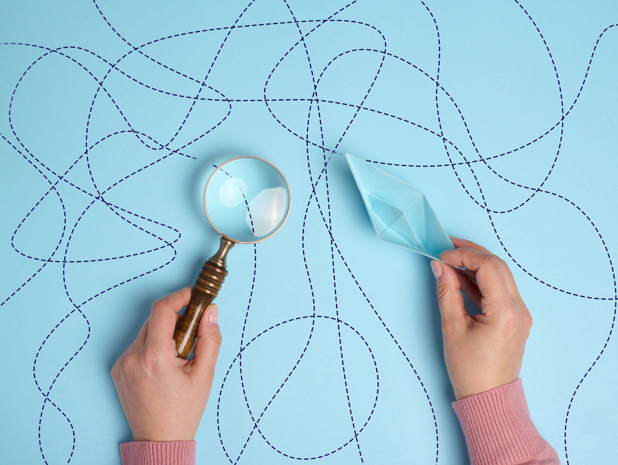 A female hand holds a paper boat and a magnifying glass, symbolizing the exploration of the path