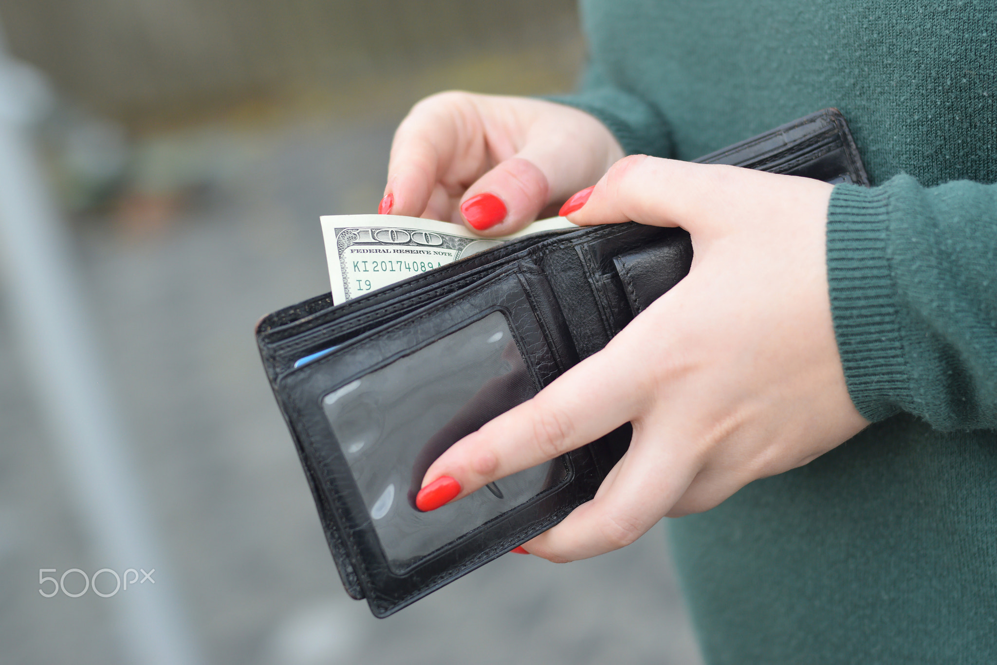 Woman hands with red nails holds black mens purse with many US hundred dollars bills. Concept of