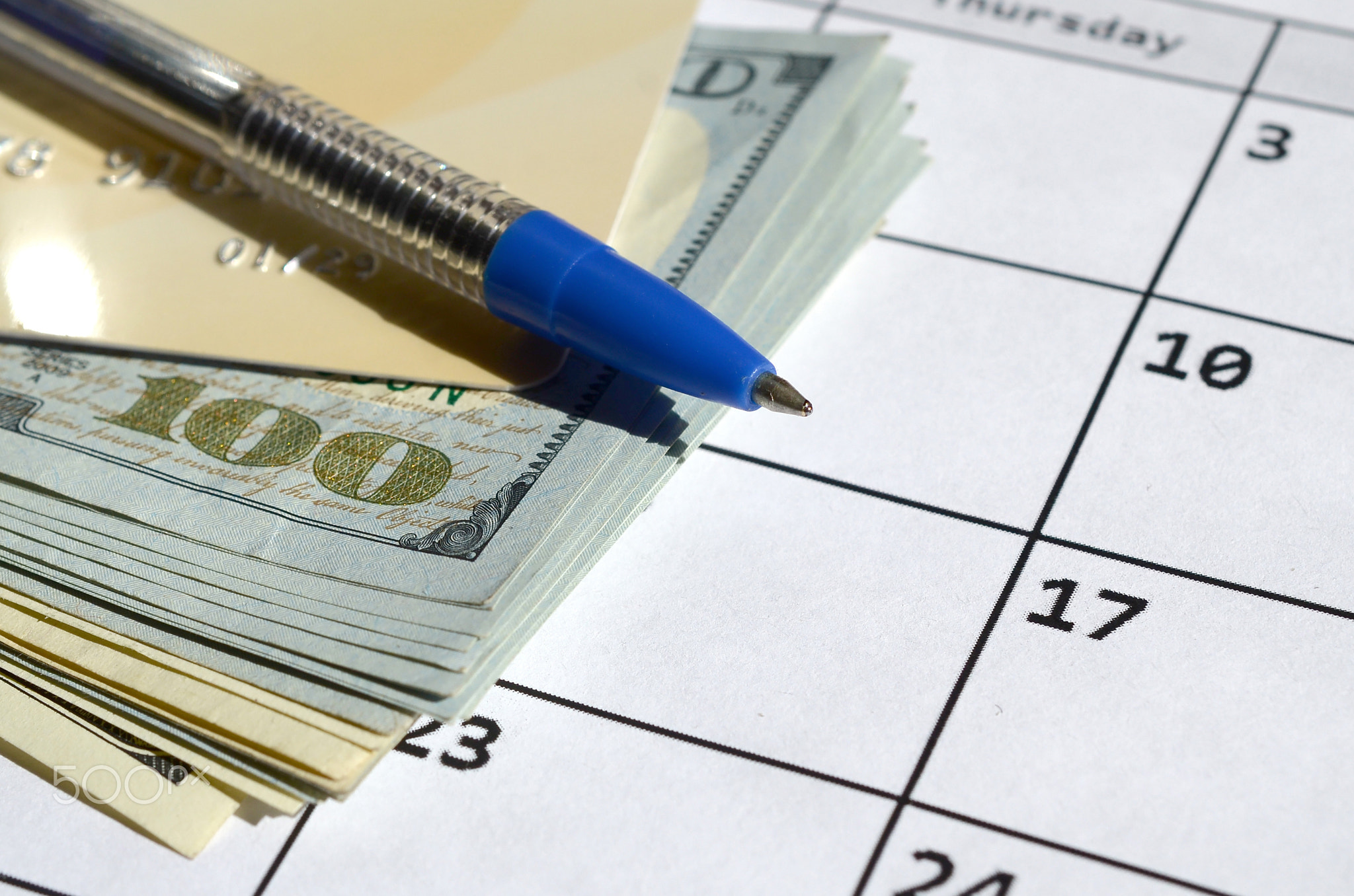 Pen and credit card on many hundred US dollar bills on calendar page close up