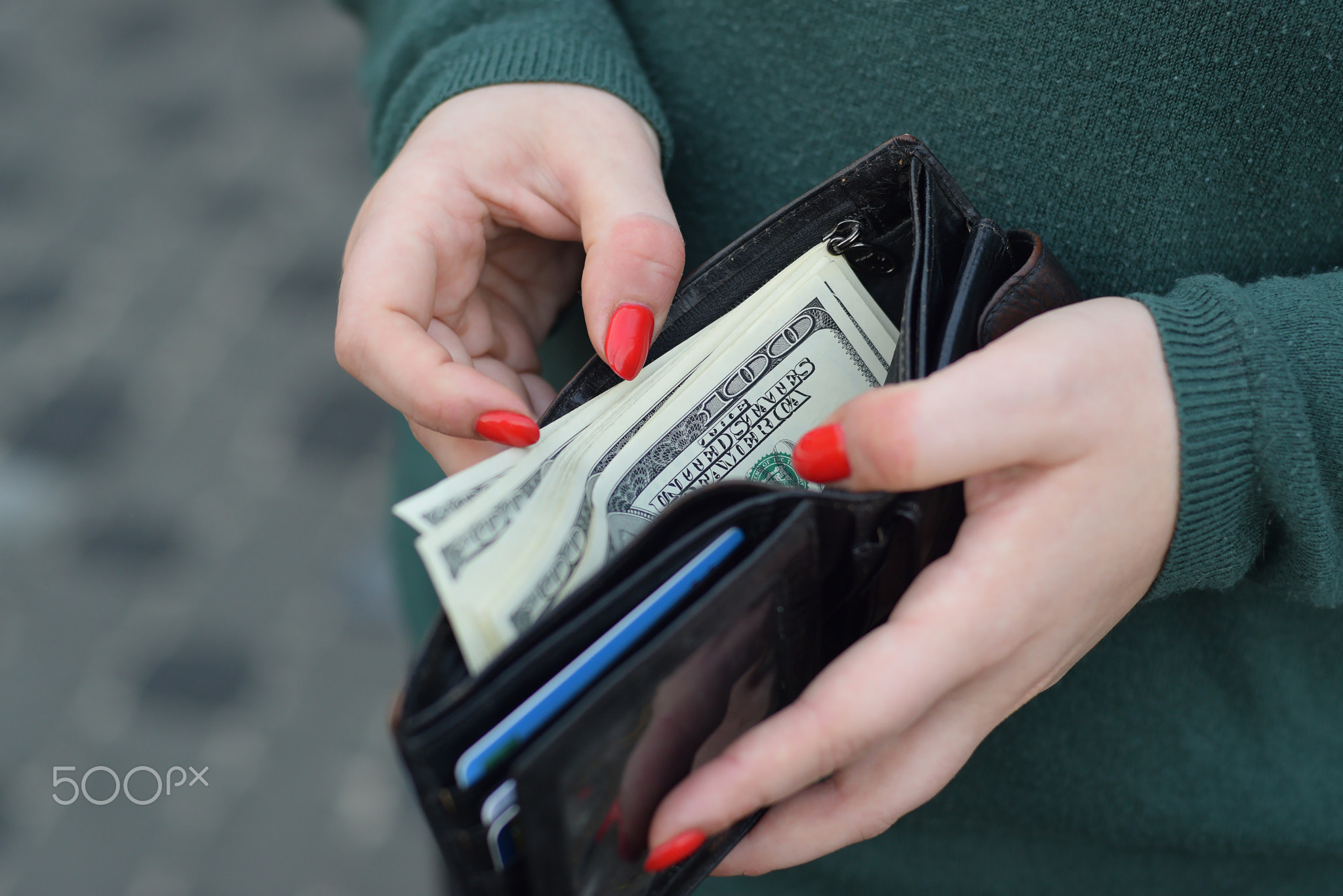 Woman hands with red nails holds black mens purse with many US hundred dollars bills. Concept of