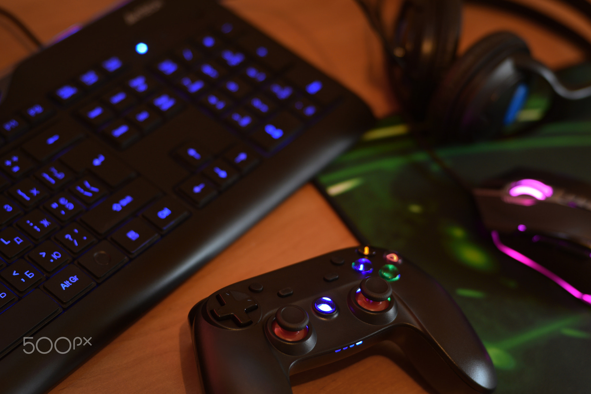Modern gamepad and gaming mouse lies with keyboard and headphones on table in dark playroom scene