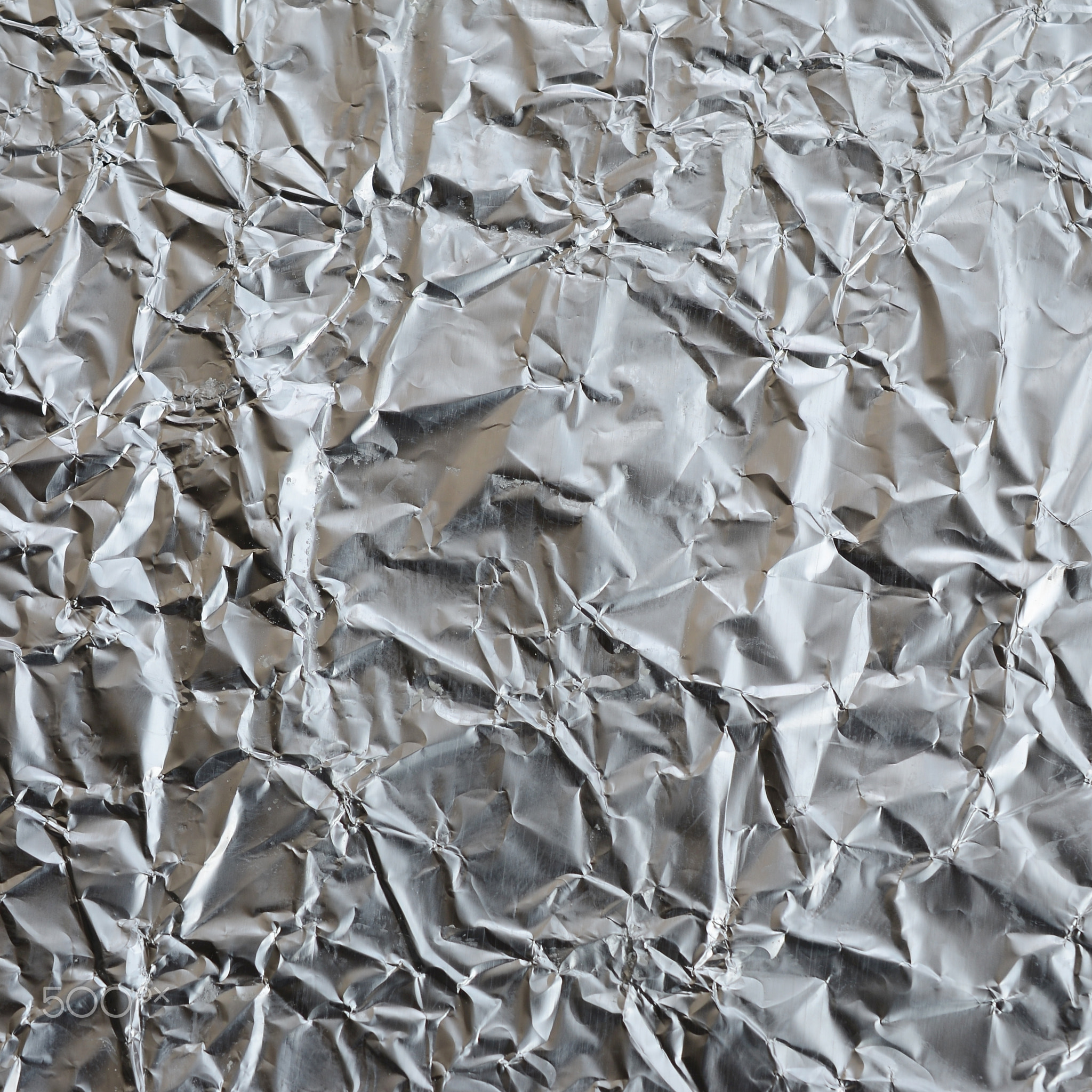 Thin wrinkled sheet of crushed tin aluminum silver foil background with shiny crumpled surface for