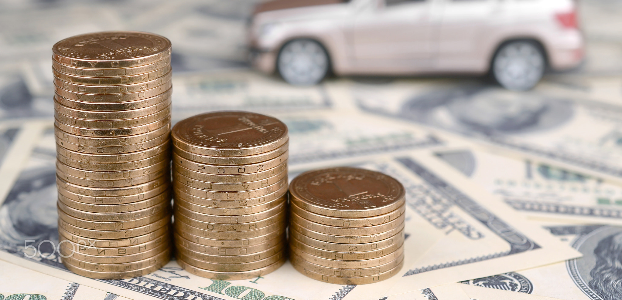 Toy car model at the stacks of golden coins lies on many dollar bills