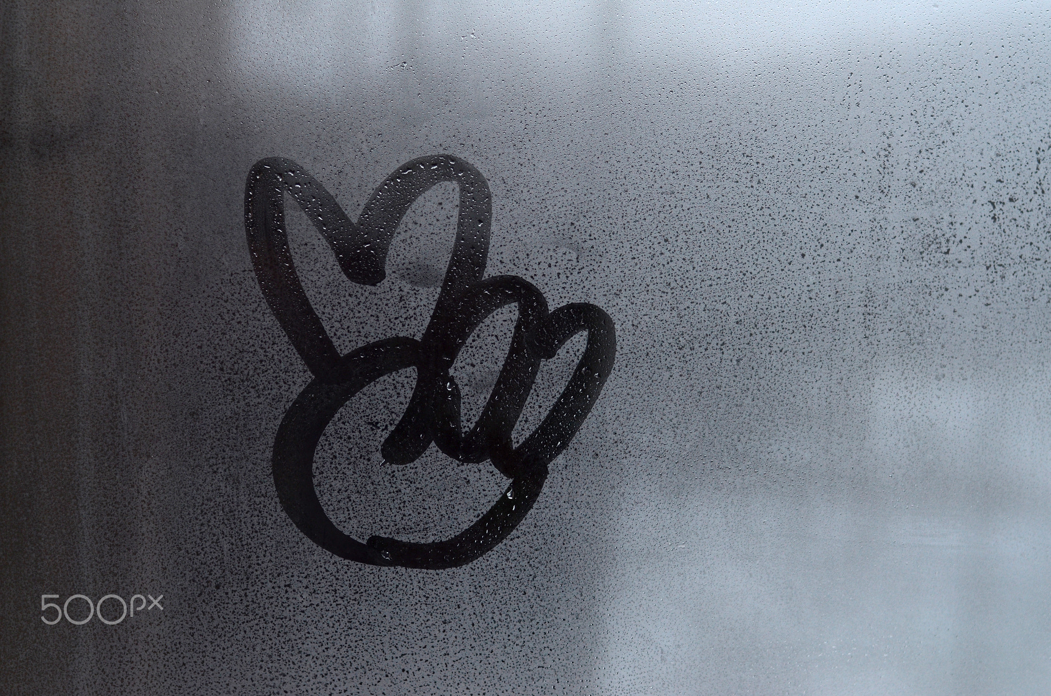 The image of the peace symbol is drawn with a finger on the surface of a misted glass window