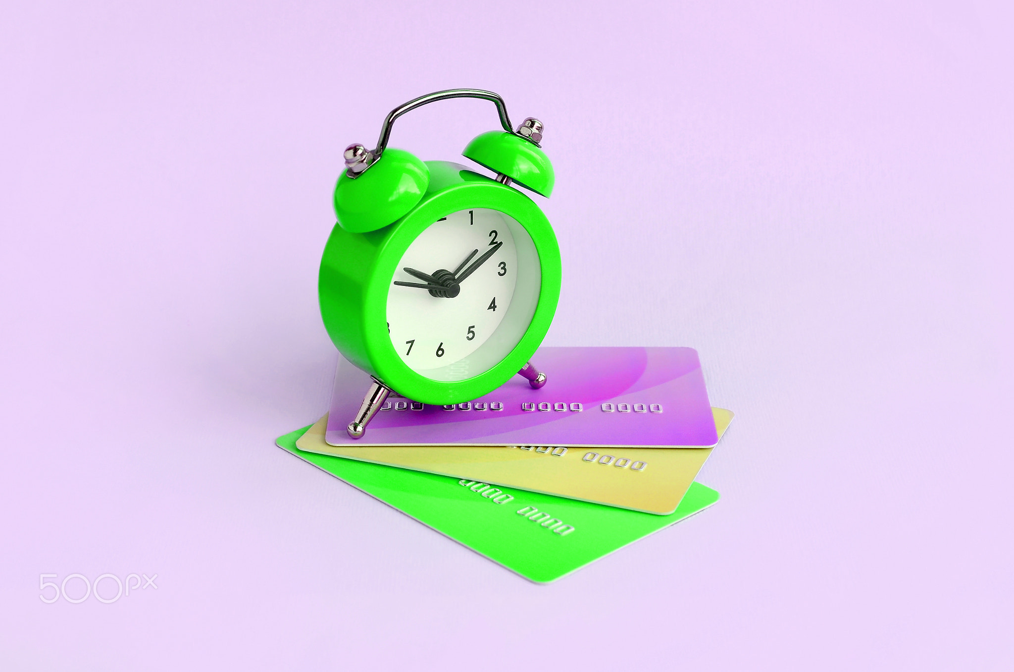 Small alarm clock lies on colored credit cards