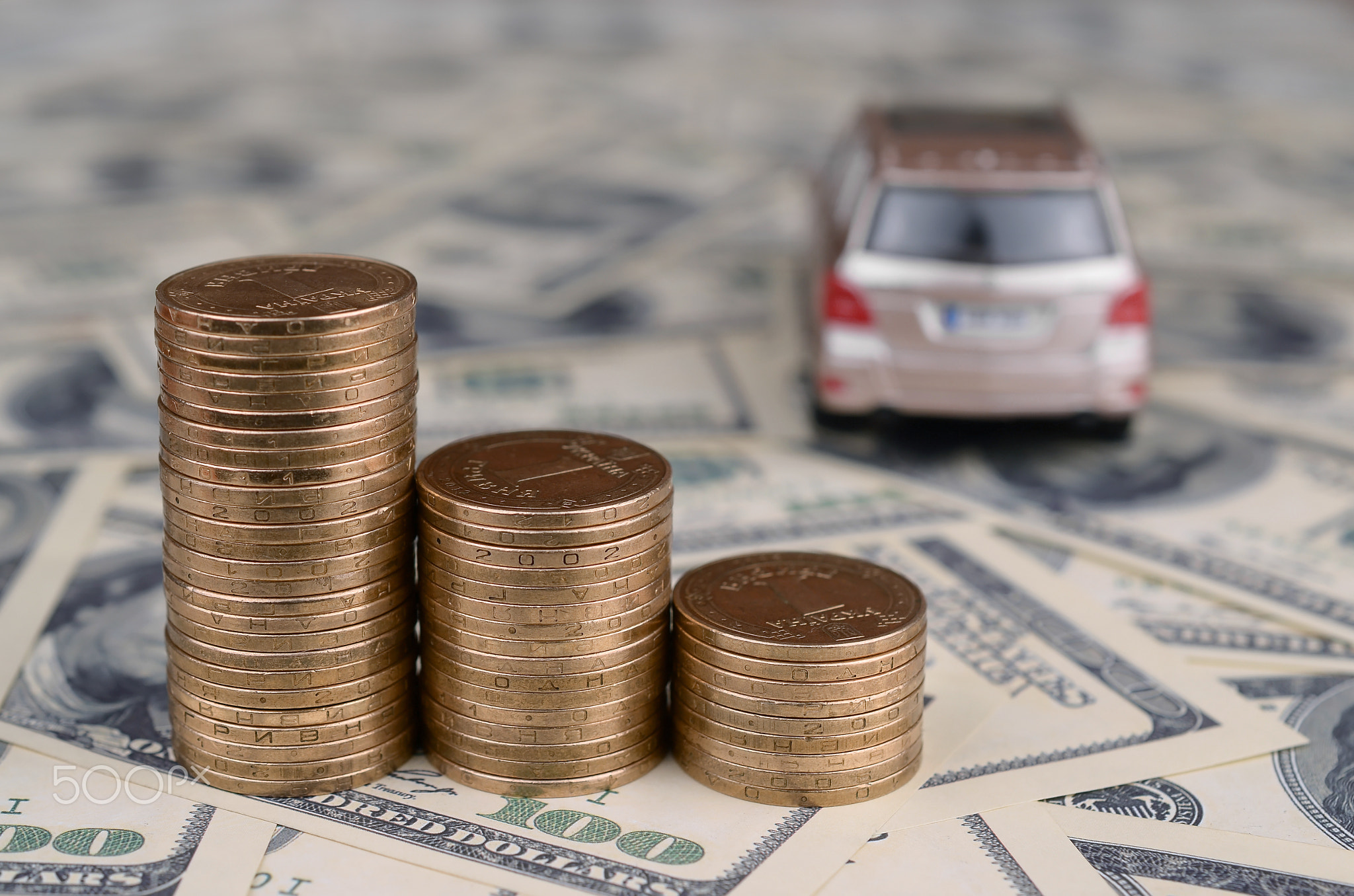 Toy car model at the stacks of golden coins lies on many dollar bills