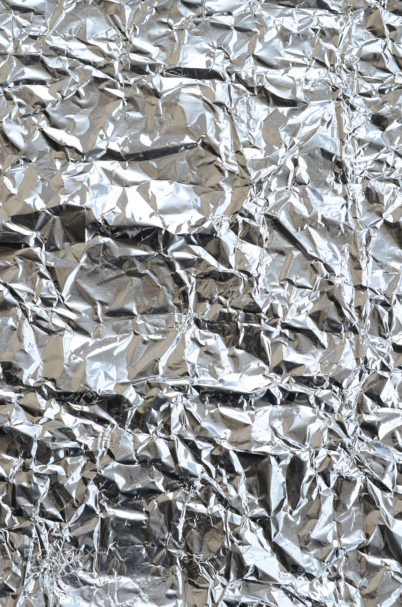 Thin wrinkled sheet of crushed tin aluminum silver foil background with shiny crumpled surface for