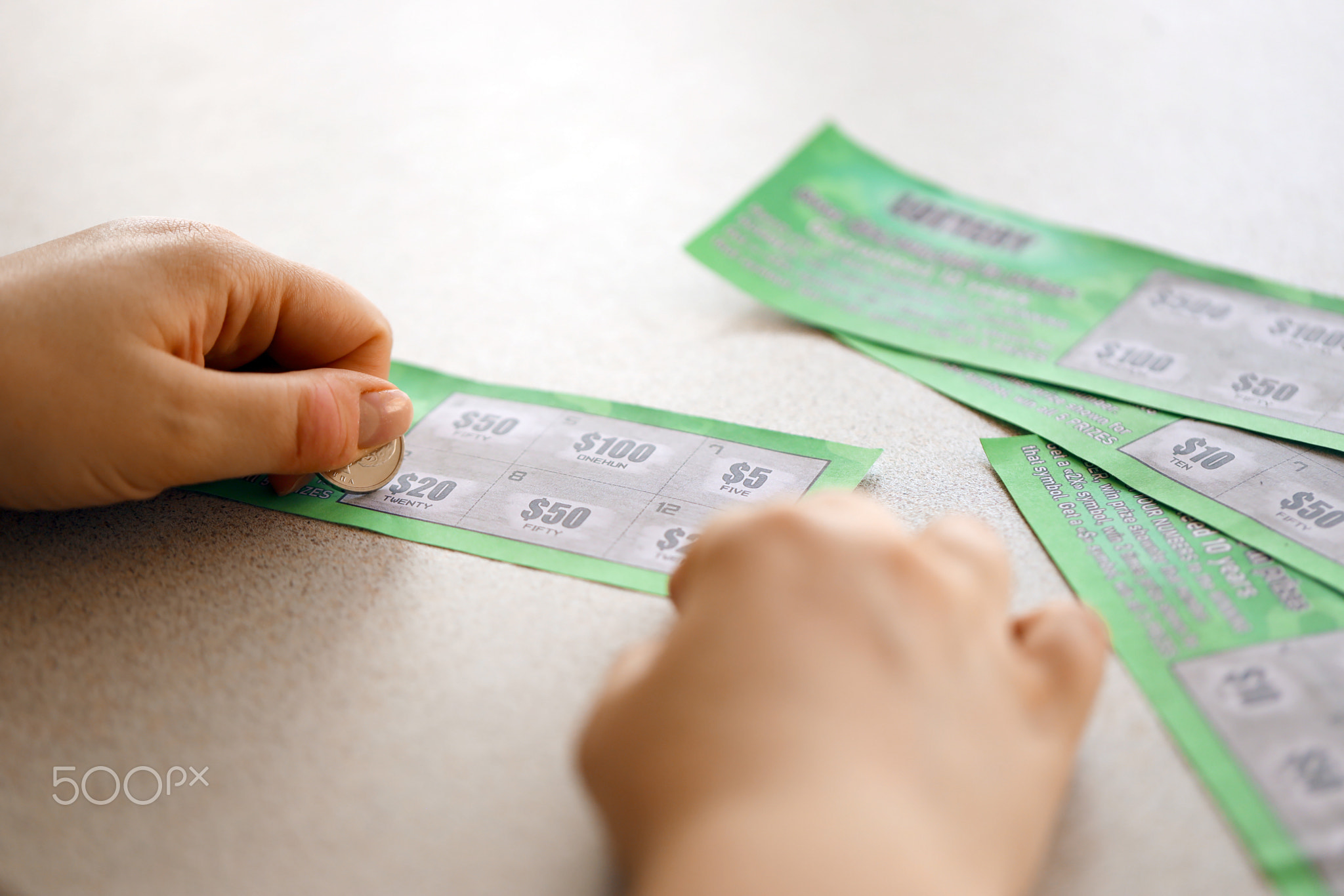 Close up view of silver coin in hand of gambler scratching fake lottery card. Lottery gambling