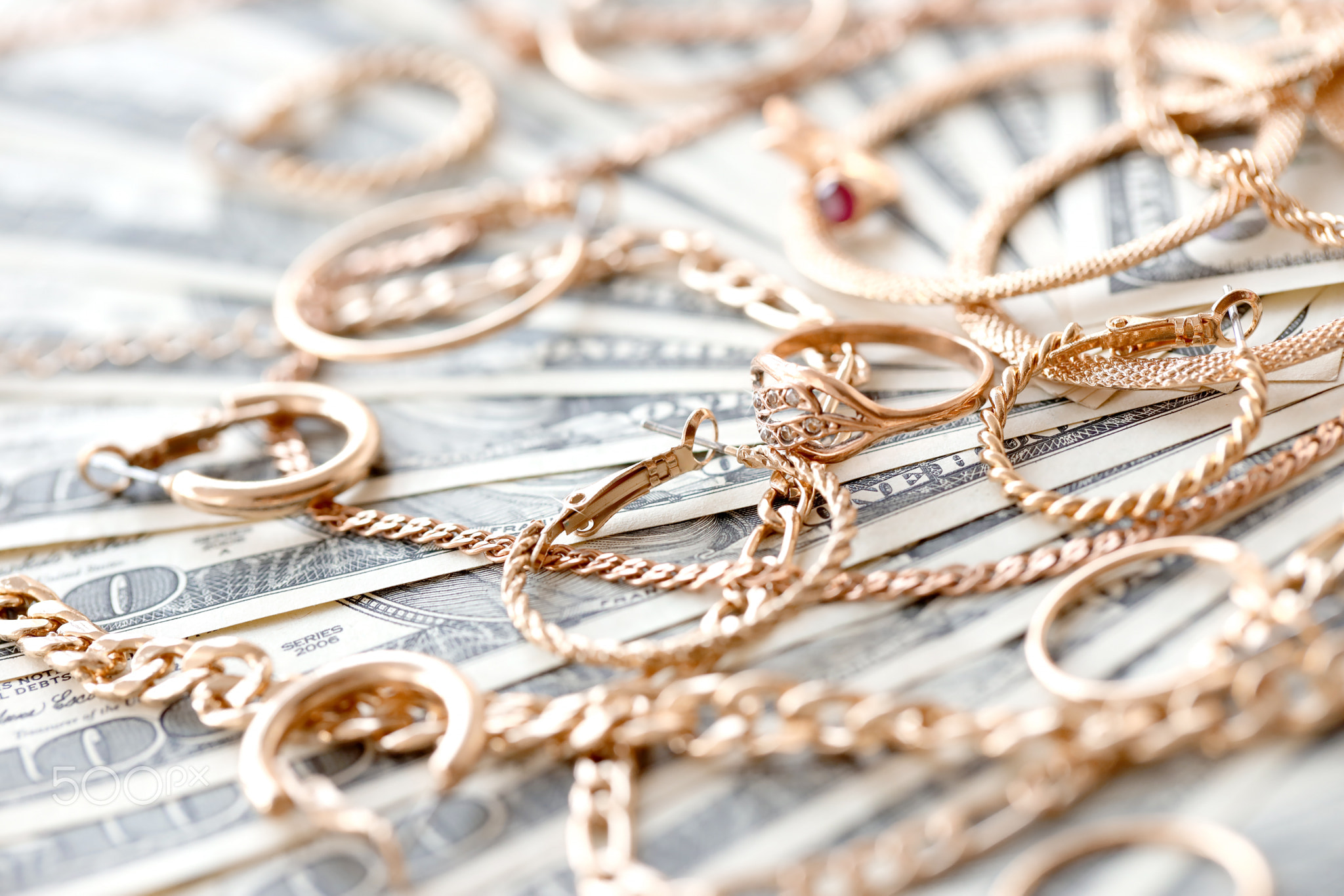 Many expensive golden jewerly rings, earrings and necklaces on big amount of US dollar bills close