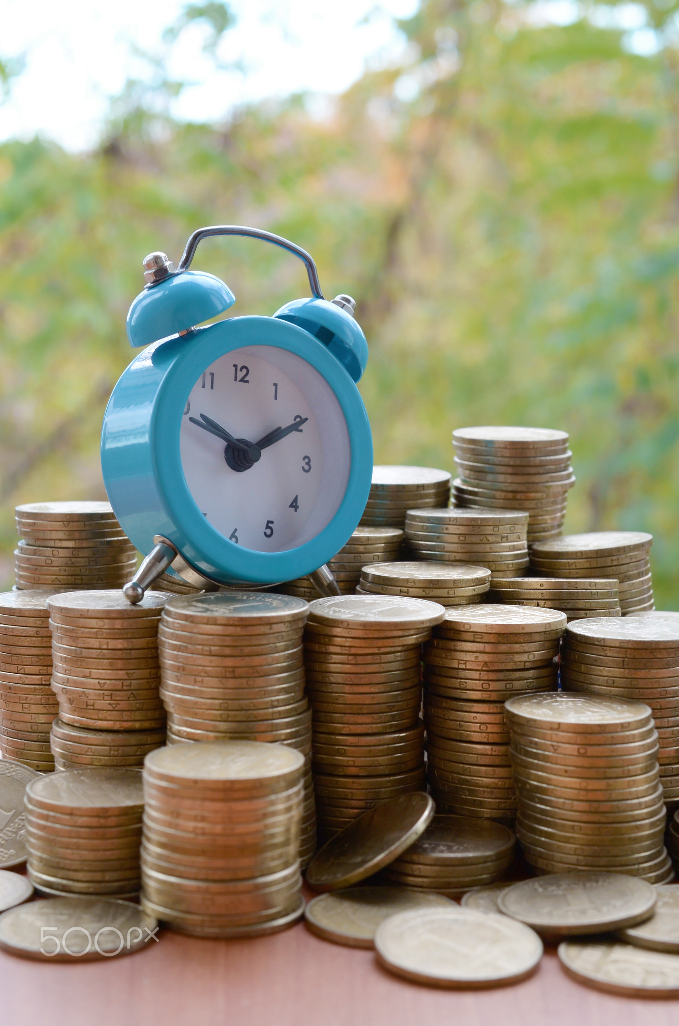 Blue alarm clock on big amount of shiny ukrainian old 1 hryvnia coin stacks close up on blurred