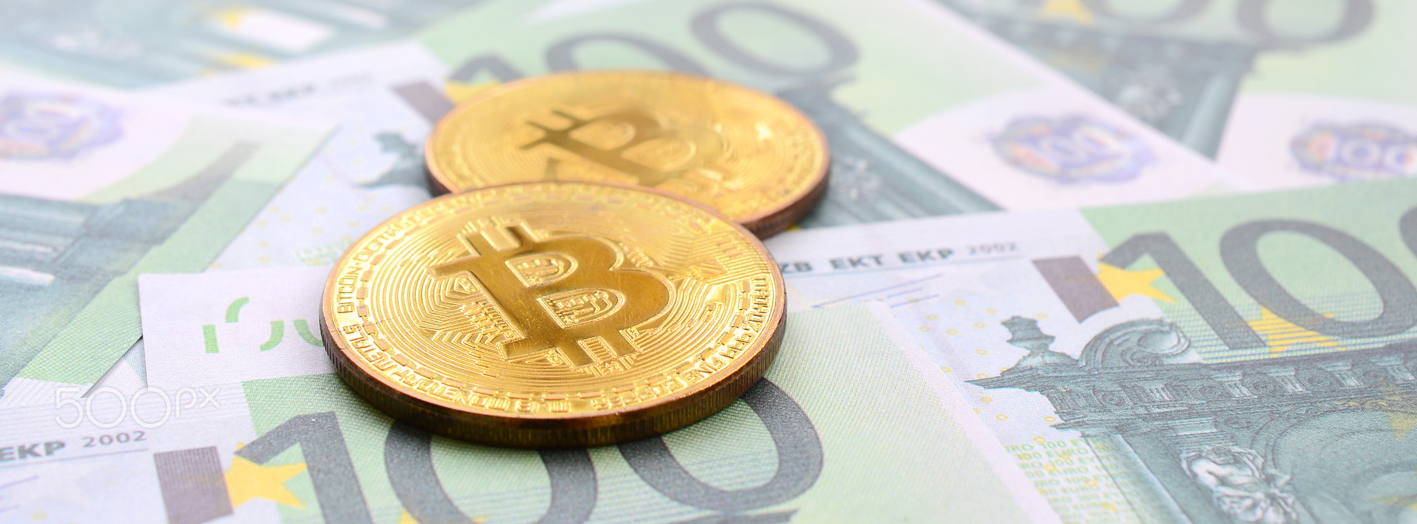 Golden physical bitcoins is lies on a set of green monetary denominations of 100 euros. A lot of